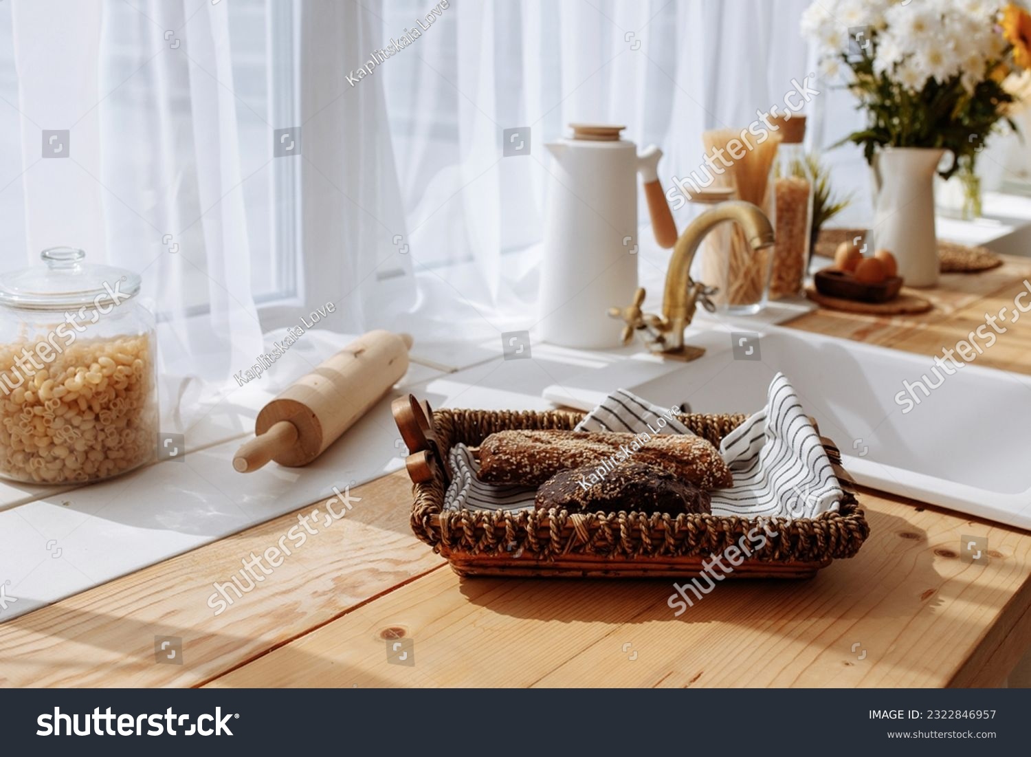 Fresh bread and utensils on the kitchen table, ready to be cooked. Simple modern scandinavian style kitchen, kitchen details, wooden table, bouquet of flowers in a vase on the table. #2322846957
