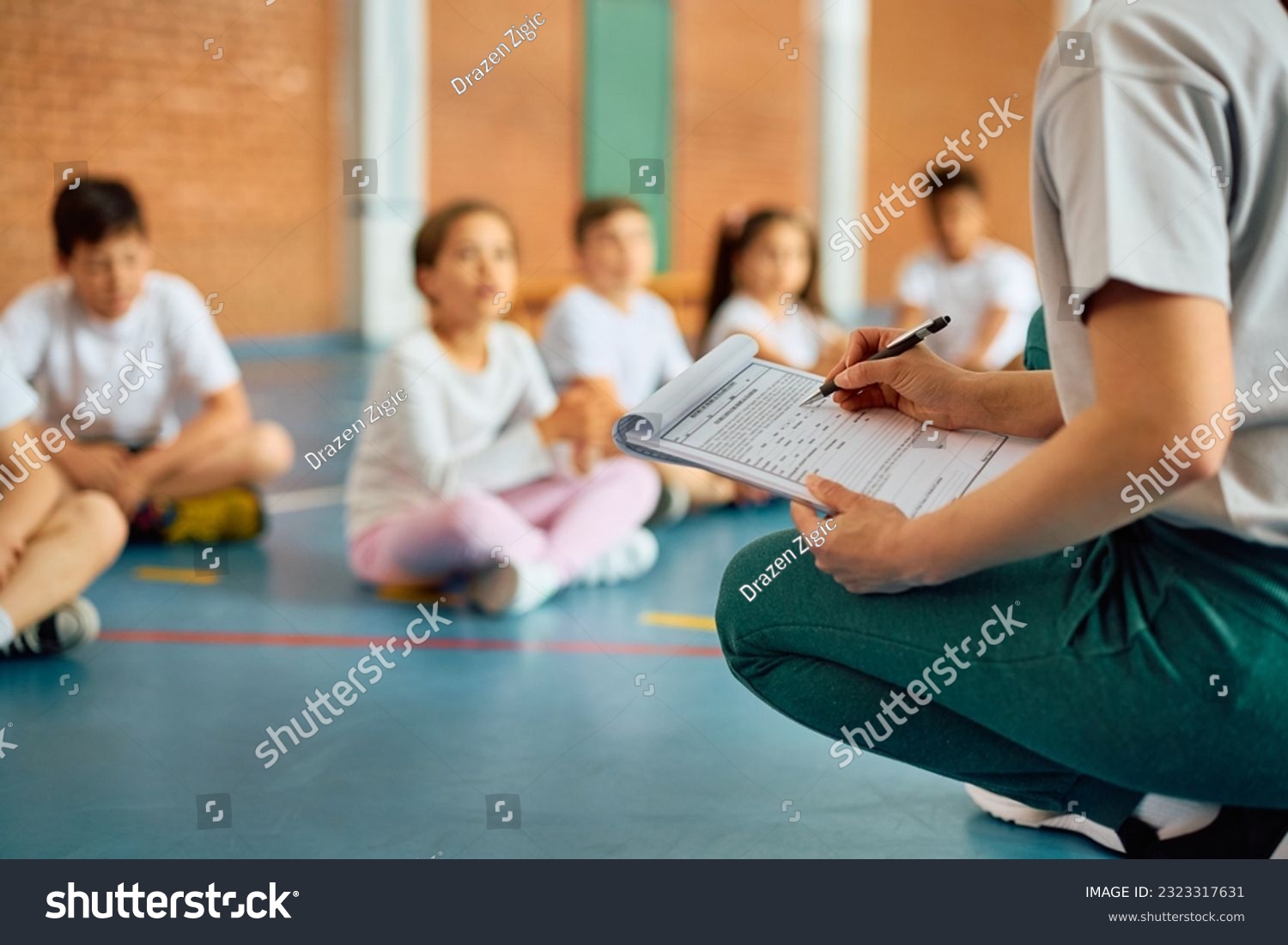 Close up of sports teacher taking notes during physical education class at school gym. #2323317631