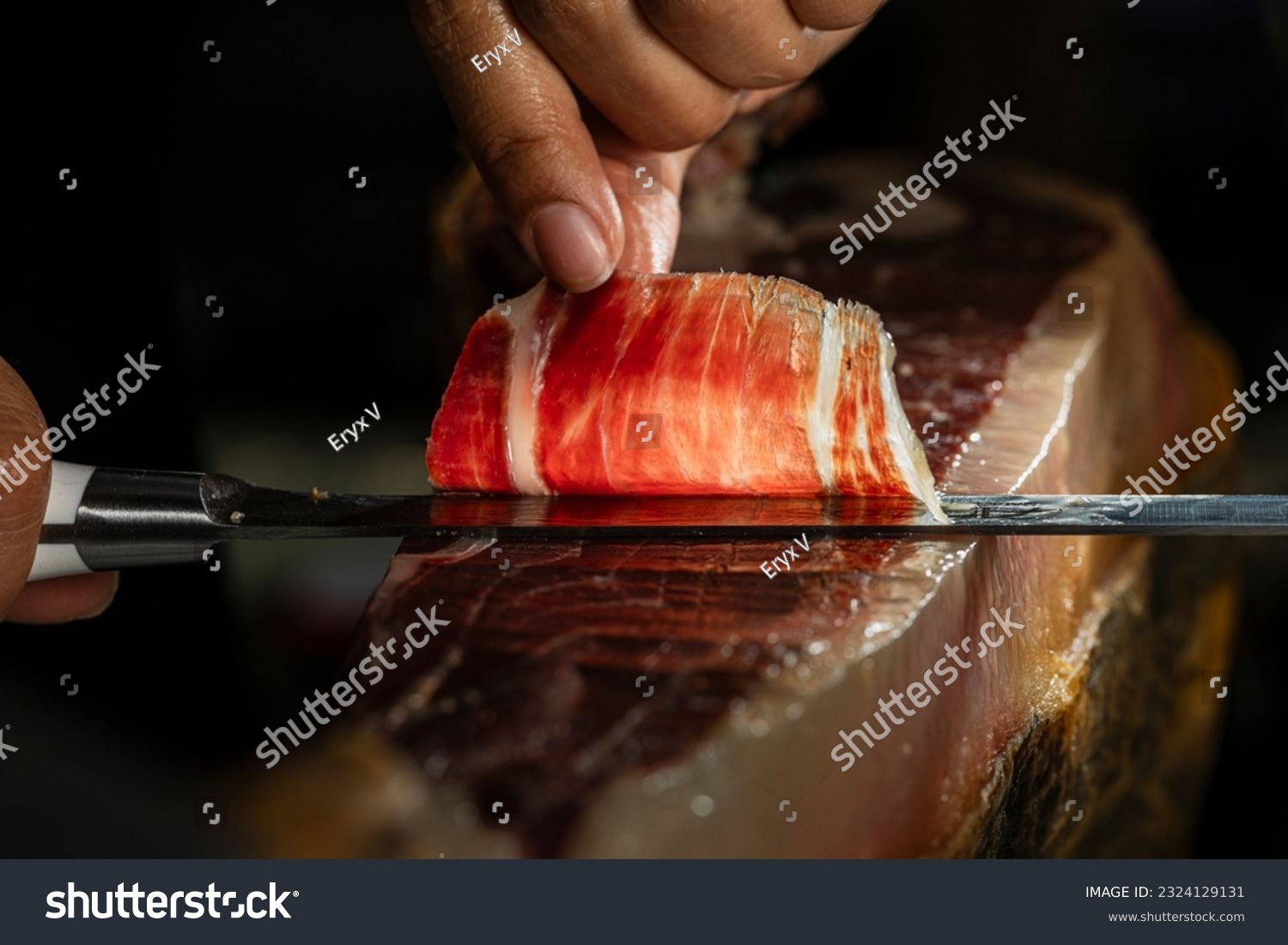 Slice of Iberian ham from Spain 100% acorn-fed, cut with a knife by a professional. Close up view of ham cutter typical of Spain gourmet product international sale #2324129131
