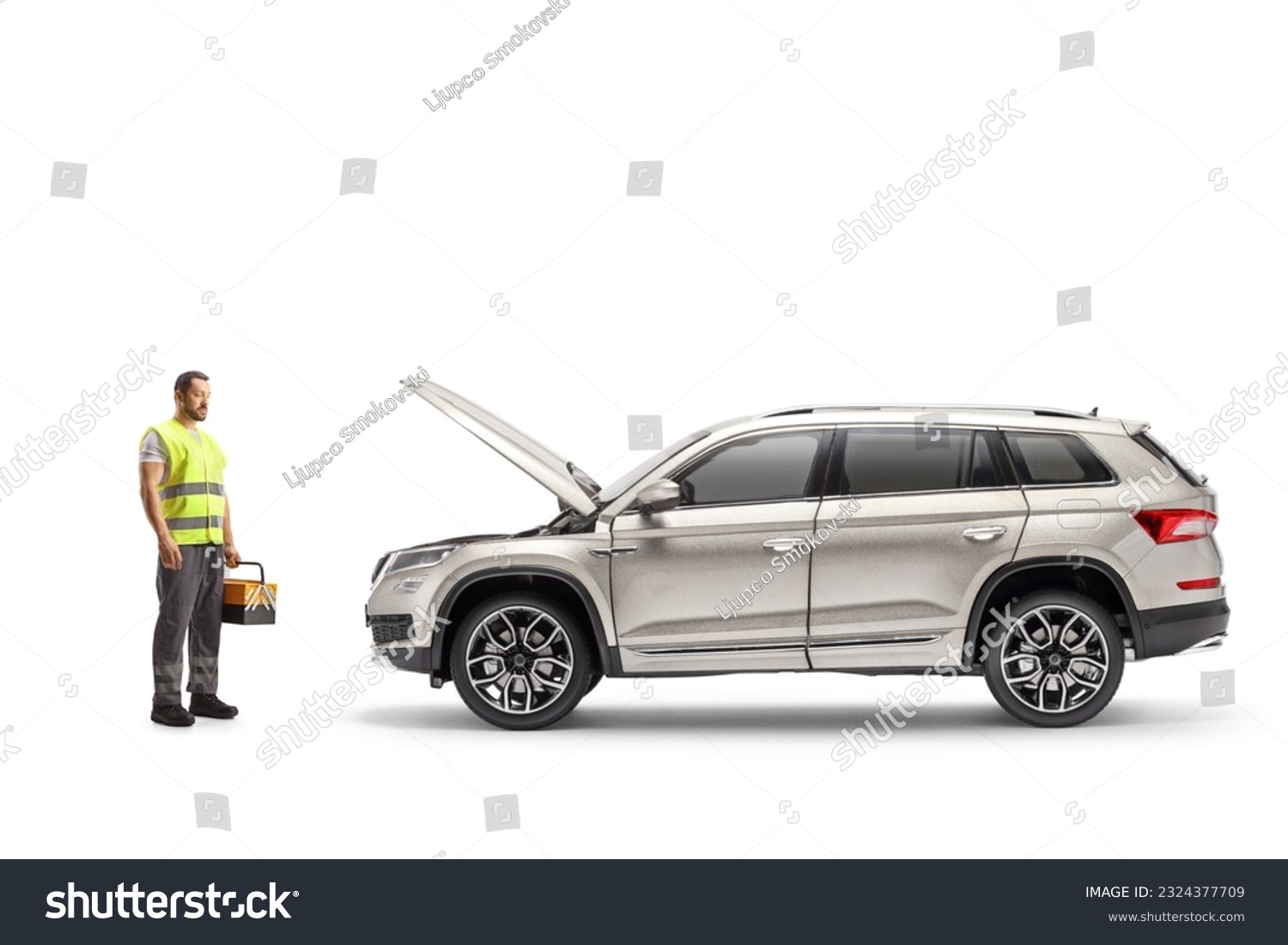 Roadside mechanic holding a tool box and looking at a vehicle with an open hood isolated on white background #2324377709