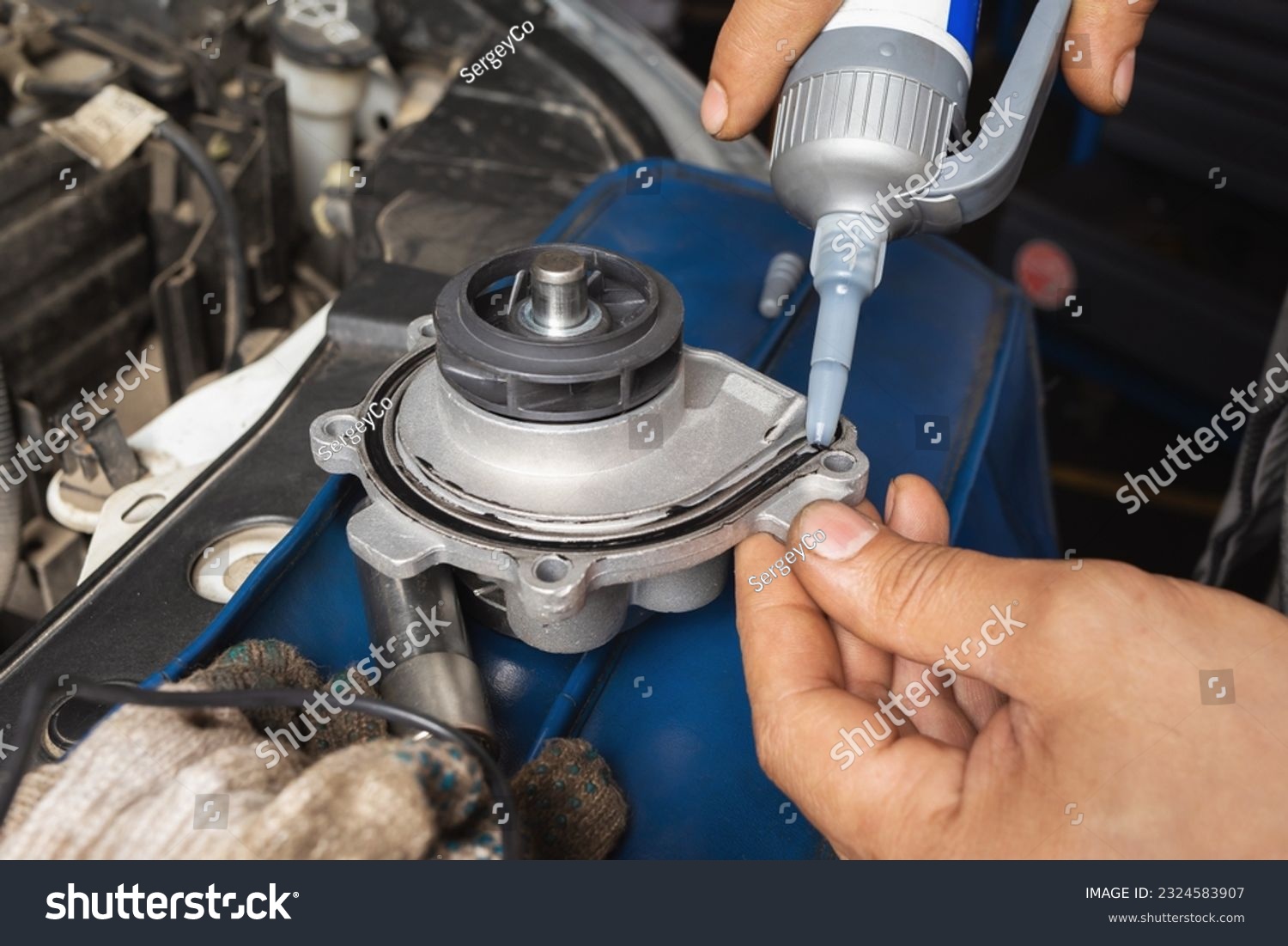 An auto mechanic applies silicone black sealant to a new engine cooling pump before installing it #2324583907