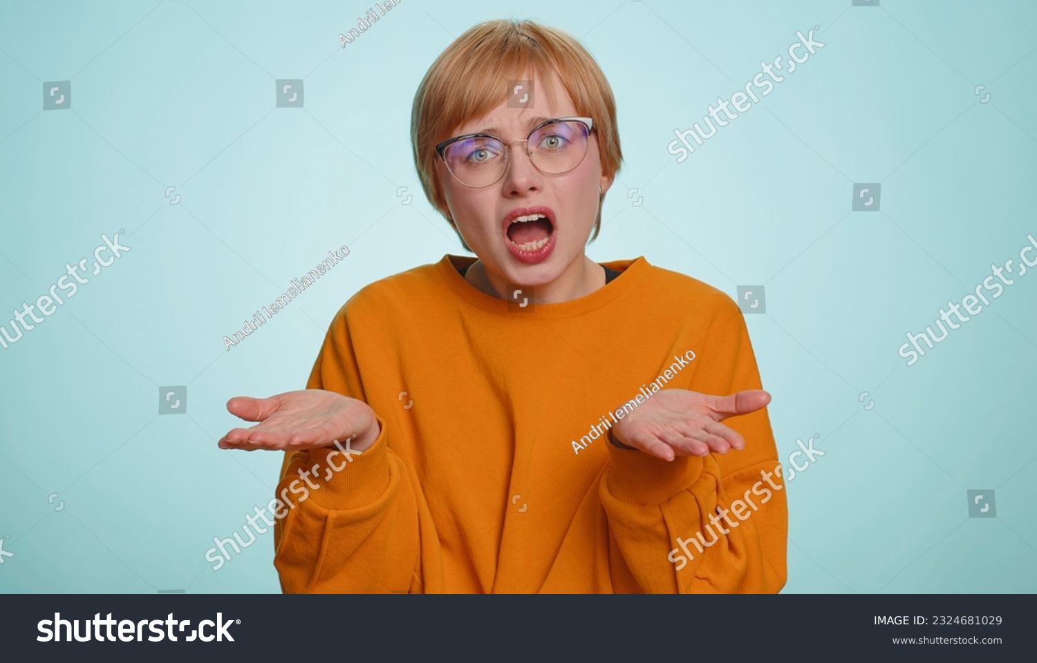 What Why. Sincere irritated woman in glasses raising hands in indignant expression, ask reason of failure demonstrating disbelief irritation by trouble. Pretty confused blonde girl on blue background #2324681029