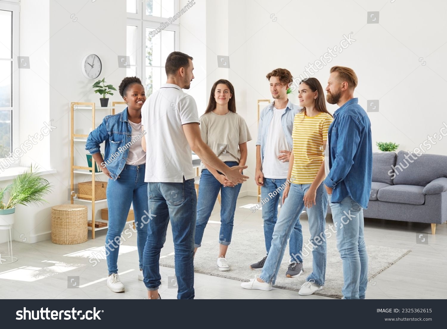 Group of diverse friends having a discussion. Several young multiracial people standing in the living room at home and listening to a young man talking about something #2325362615