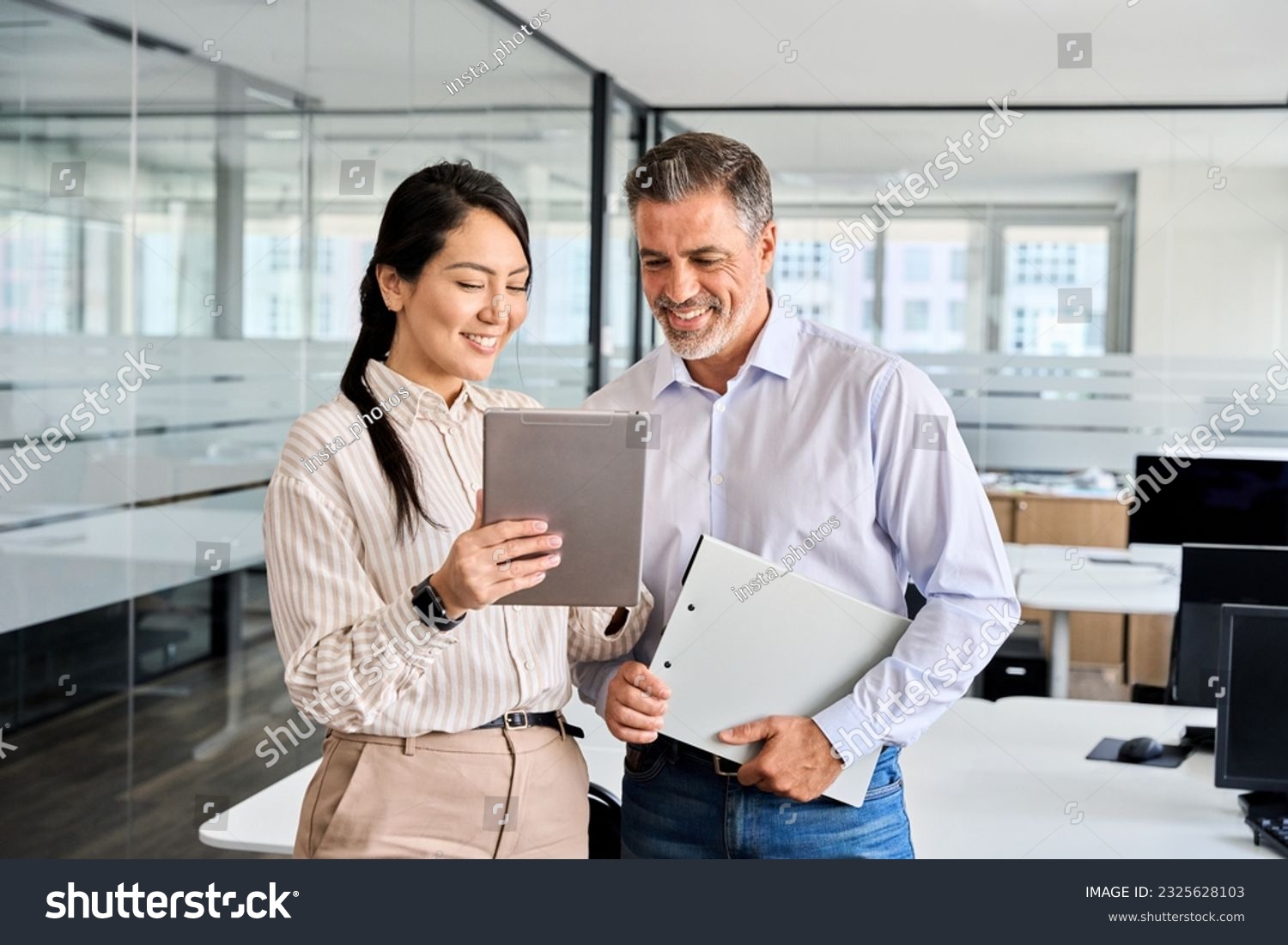 Two happy professional business people team Asian woman and Latin man workers working using digital tablet tech discussing financial market data standing at corporate office meeting. #2325628103