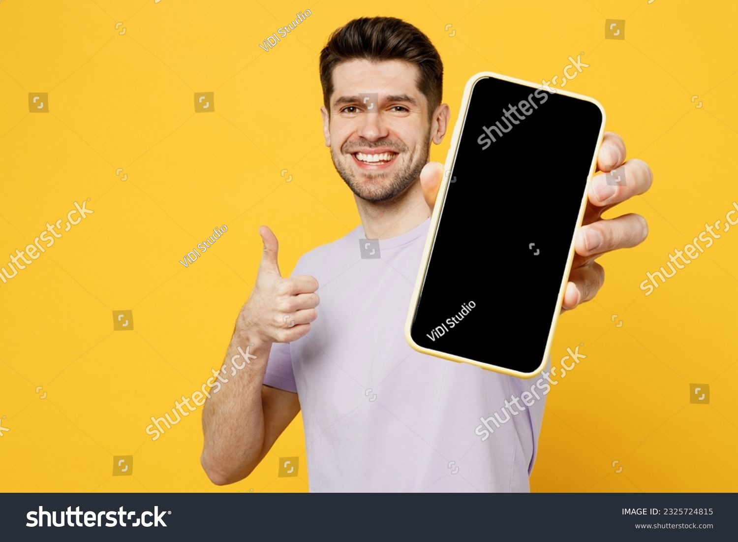 Young man wear light purple t-shirt casual clothes hold in hand use close up mobile cell phone with blank screen workspace area isolated on plain yellow background studio portrait. Lifestyle concept #2325724815