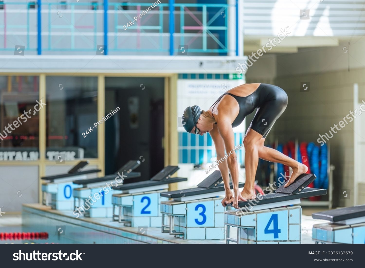 Elite female swimmer taking a position on the start block, using slingshot technique with a back footplate. Professional sport concept. #2326132679