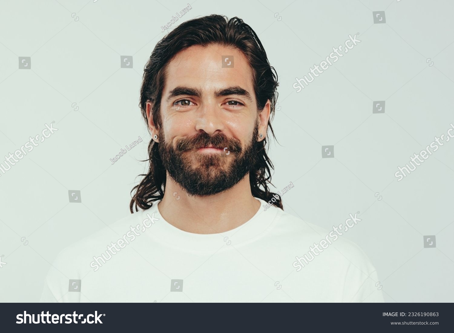Portrait of a confident young man looking at the camera in a studio, proudly wearing a beard and long hair. Man with a beautiful appearance embracing his personal grooming and self-care. #2326190863
