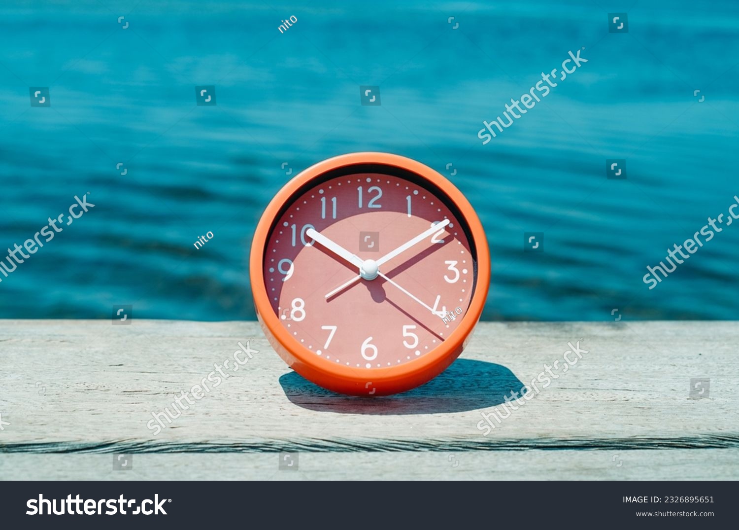 closeup of a pink clock on a weathered wooden pier, next to the water, on a summer day #2326895651