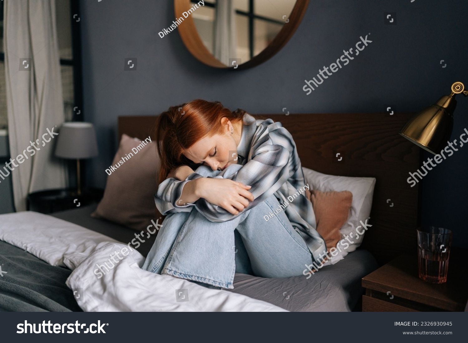 Portrait of sad upset millennial redhead female sitting on bed embrace knees lost in bad pessimistic thoughts suffer alone. Stressed young woman feel lonely desperate has broken heart. #2326930945