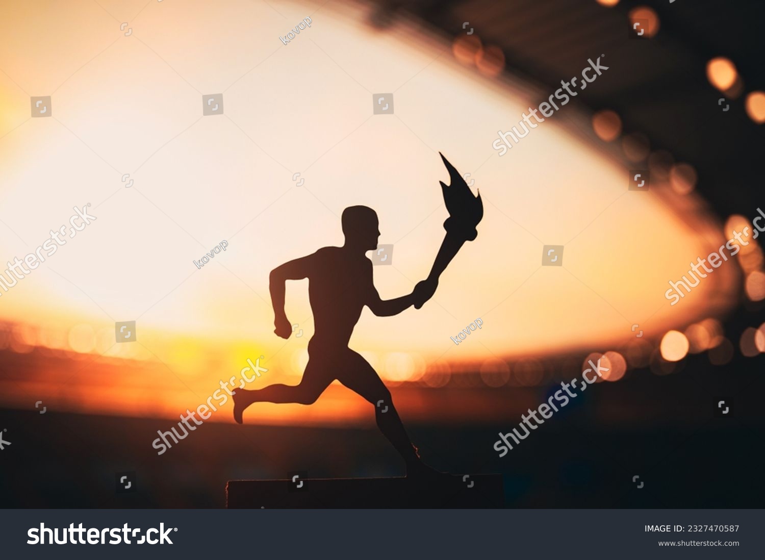 Silhouette of Male Athlete Carrying the Torch Relay, Illuminating the Modern Track and Field Stadium. A Captivating Snapshot for the Summer Game 2024 in Paris. #2327470587