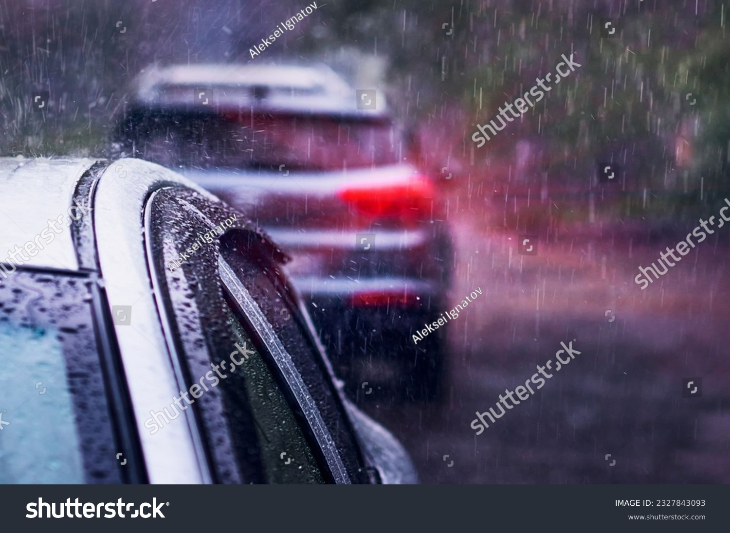 Heavy rain falls on the roof of a car during a thunderstorm. Red brake light in the dark. The concept of auto insurance and natural disasters. Driving on cloudy rainy days. Selective focus. #2327843093