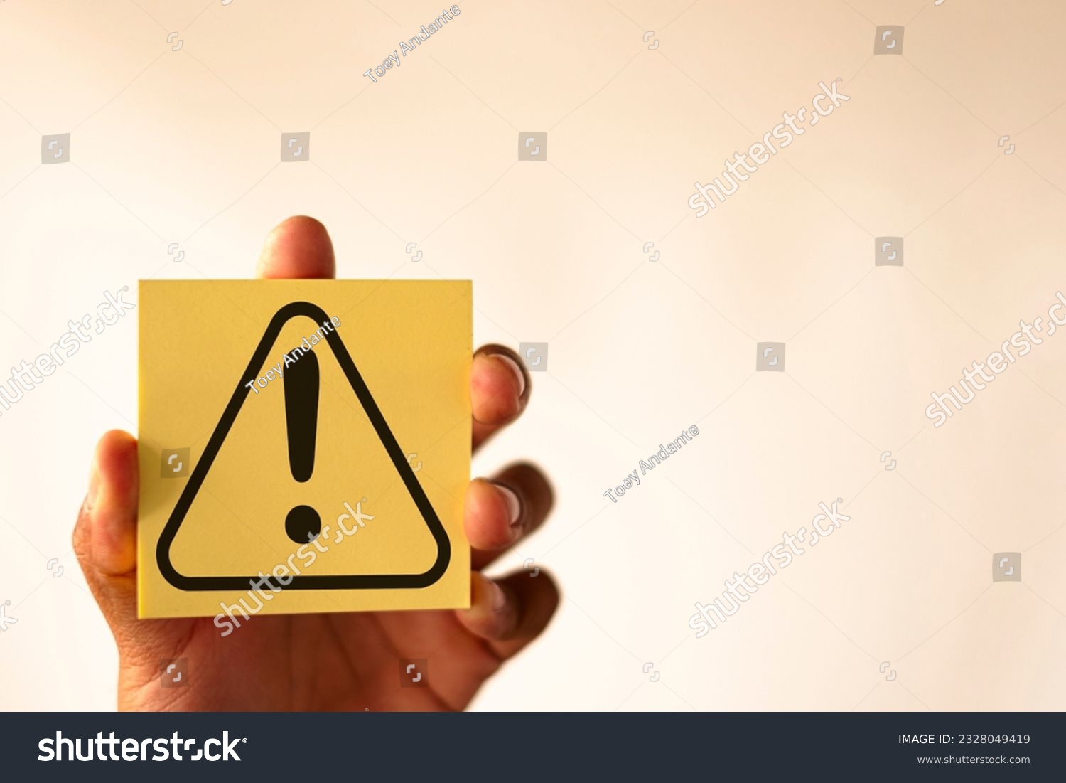 Hand holding yellow page with Exclamation mark or Warning sign over white background with copyspace concept for attention symbol,Cautionary Warning,safety, hazard,,caution, danger. #2328049419