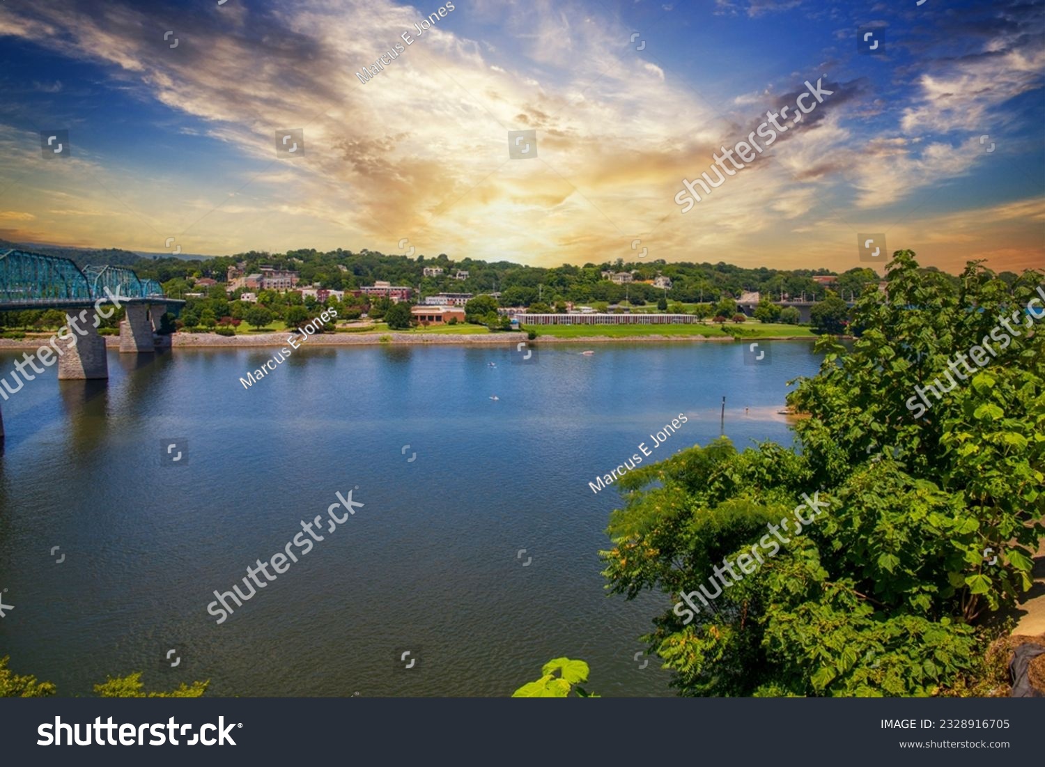 a beautiful summer landscape at the along the Tennessee River at the Walnut Street Bridge with rippling water and lush green tree and plants and powerful clouds at sunset in Chattanooga Tennessee USA #2328916705