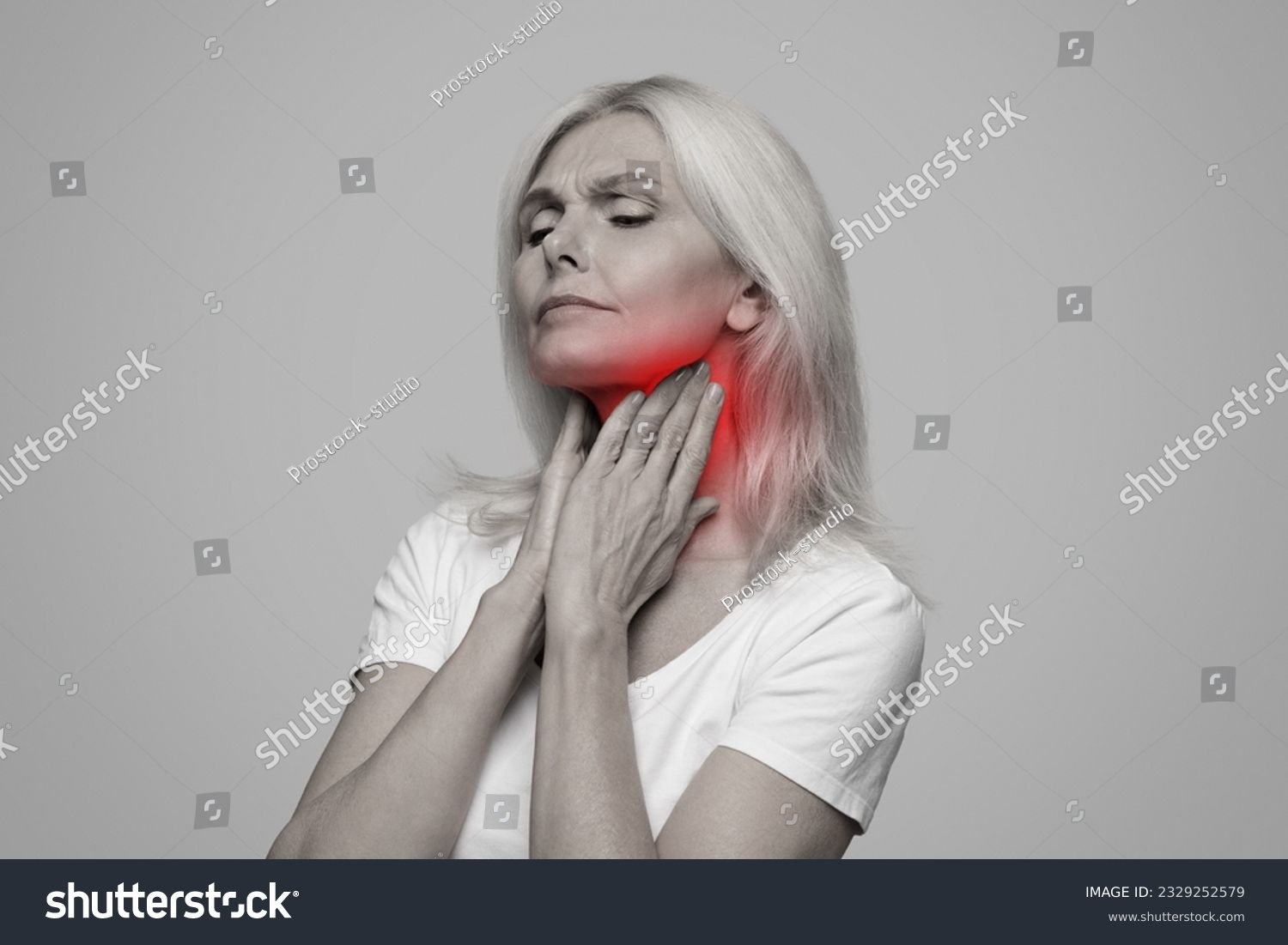 Sick mature lady having sore throat, touching her neck with red inflamed zone, suffering from laryngeal disorder, tonsillitis, throat cancer, cold, posing on studio background, black and white photo #2329252579