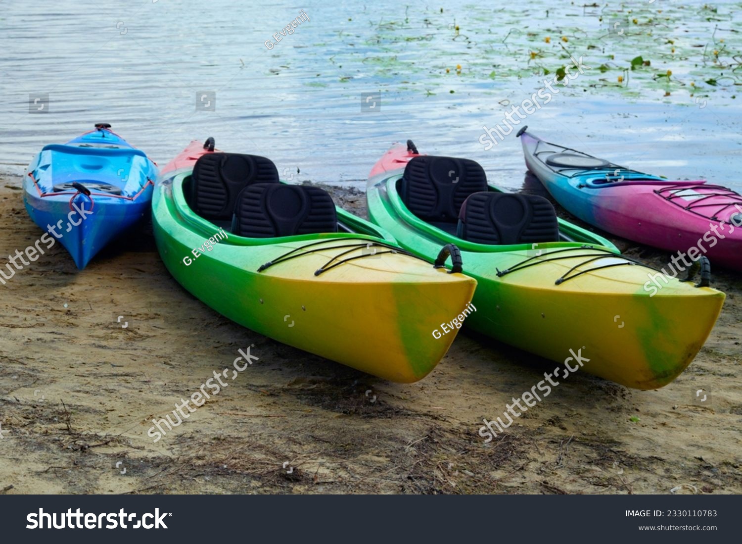 Landscape view of several colorful kayaks at the river shore. Boats on the city sandy beach, Obolon, Kyiv, Ukraine. Colorful kayaking equipment on a sandy beach. #2330110783