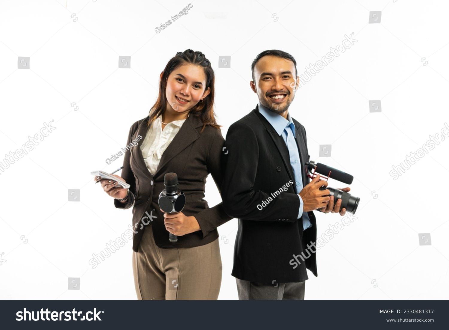 a beautiful journalist with long brown hair wearing brown blazer standing next to the male journalist in blue shirt and black suit #2330481317