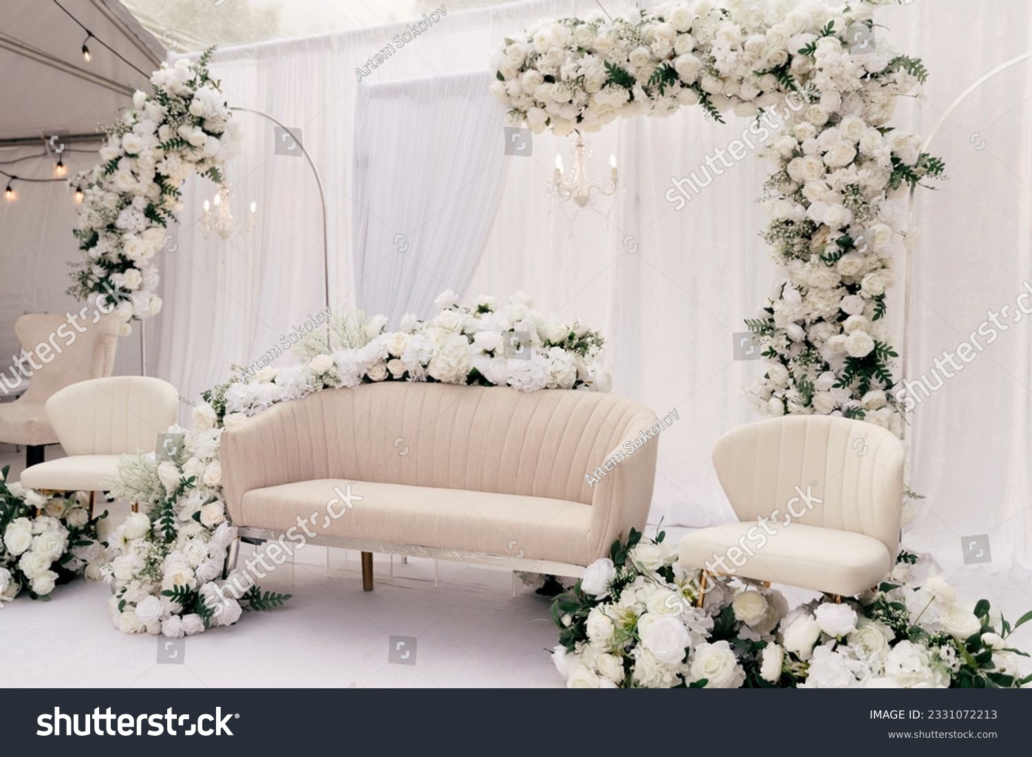 Beautiful decor for the wedding ceremony in the form of a sofa and white flowers on the ceremonial arch. Light furniture in the form of a sofa and chairs in a white tent is decorated with white roses #2331072213