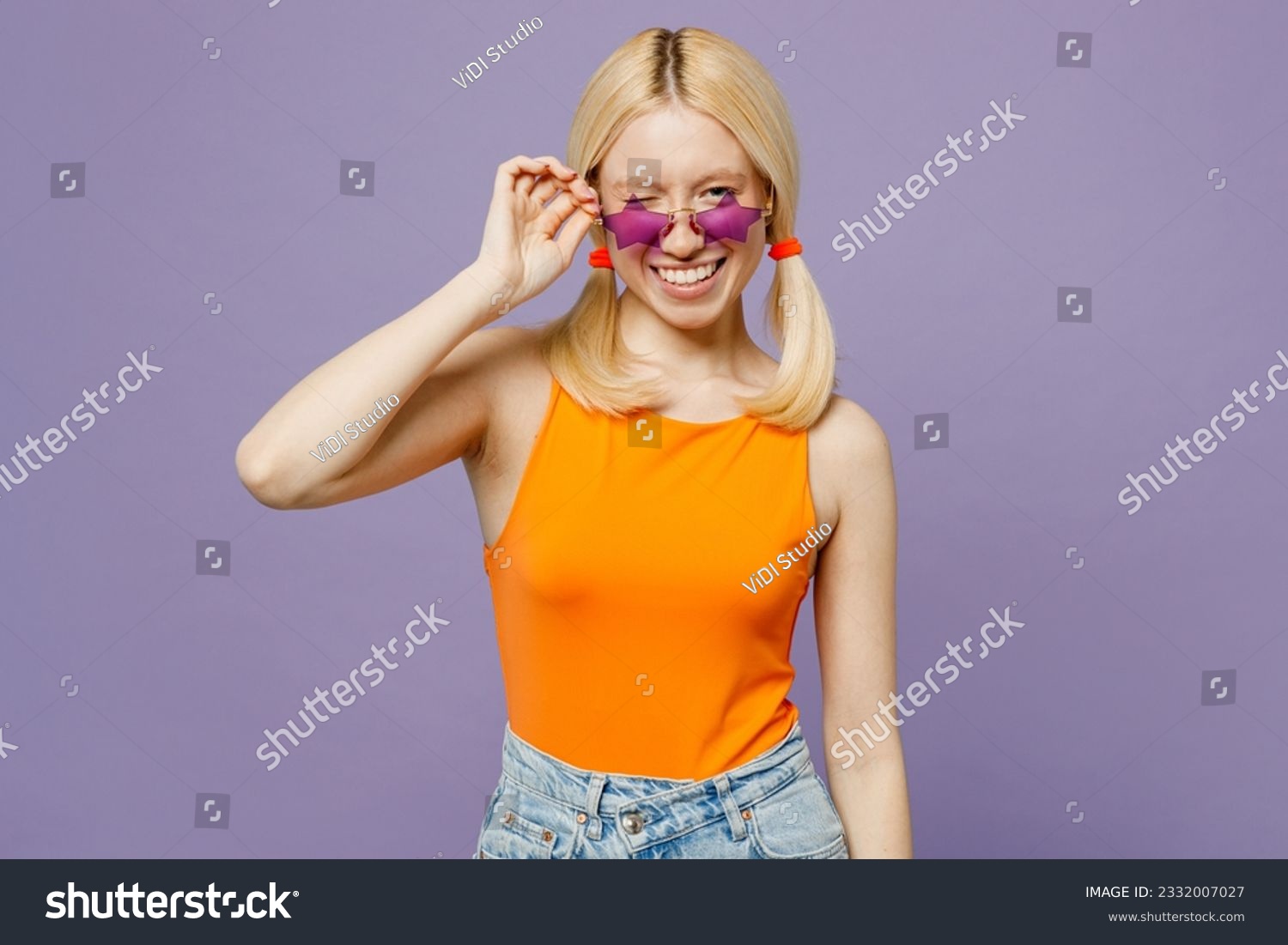 Young satisfied cheerful fun european blonde woman wears orange tank shirt casual clothes star shape sunglasses wink isolated on plain pastel light purple background studio portrait. Lifestyle concept #2332007027