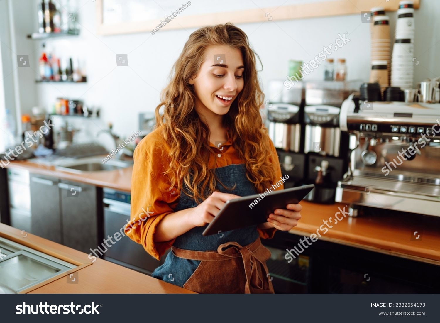 Beautiful woman owner stands behind the counter of a coffee shop. A barista with a digital tablet takes an order. Business concept. Takeaway food. #2332654173