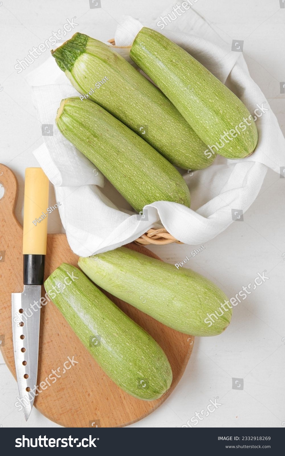 Bowl and board with fresh green zucchini on white wooden background #2332918269