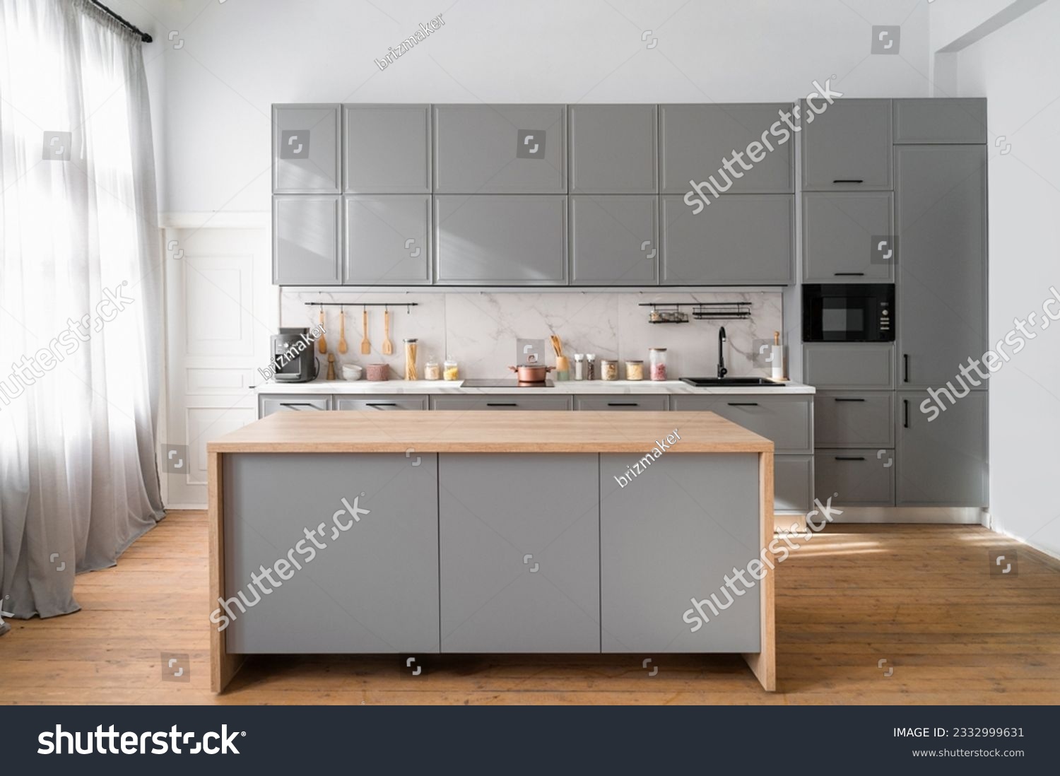 Bright minimalistic kitchen interior with gray furniture and big dining table on wooden floor. Cooking utensils and jars with food on countertop. #2332999631