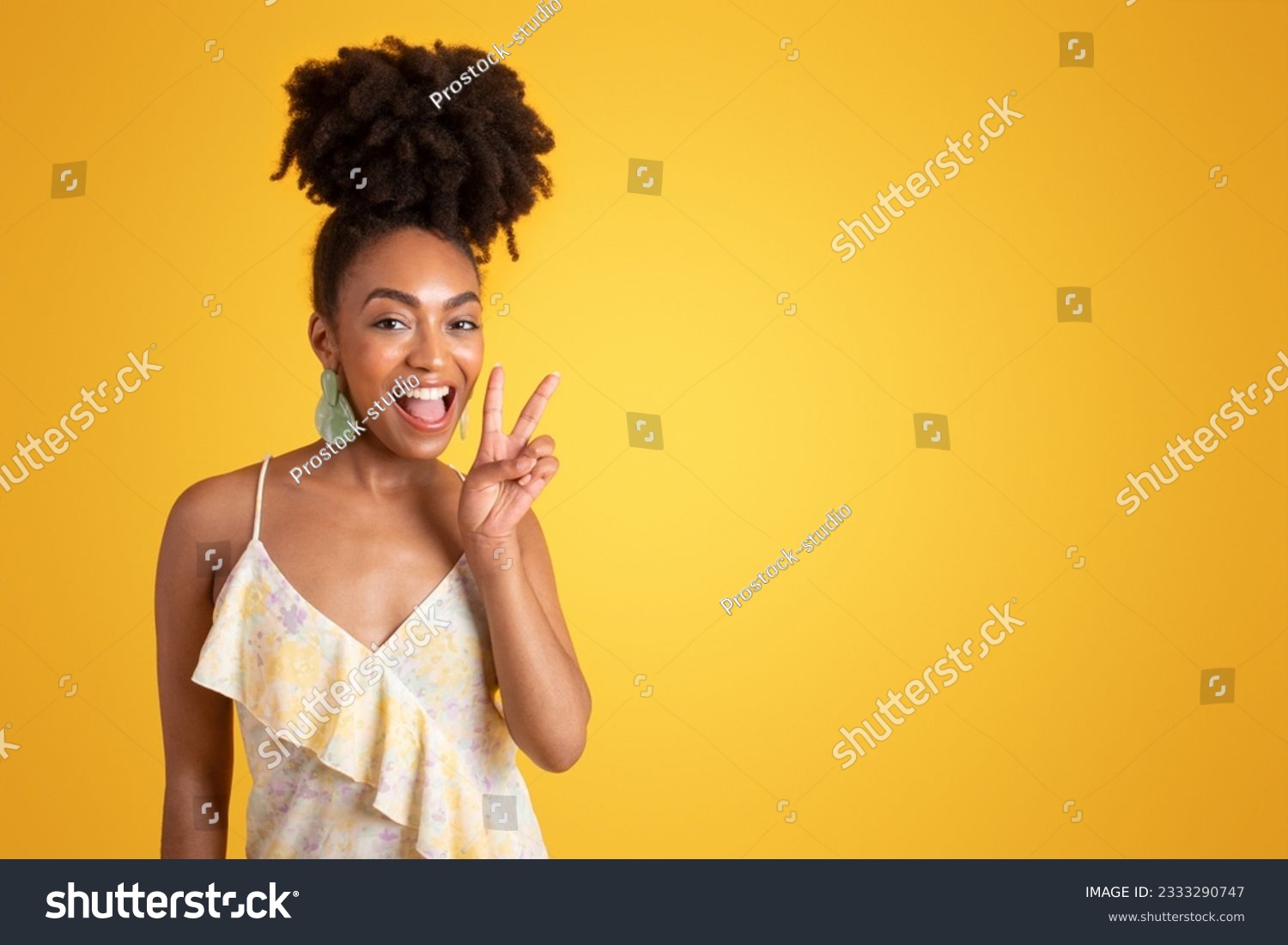 Glad young black woman in dress with open mouth making peace sign with hand, isolated on yellow background, studio. Lifestyle recommendation, good news gesture, fun emotions, ad and offer #2333290747
