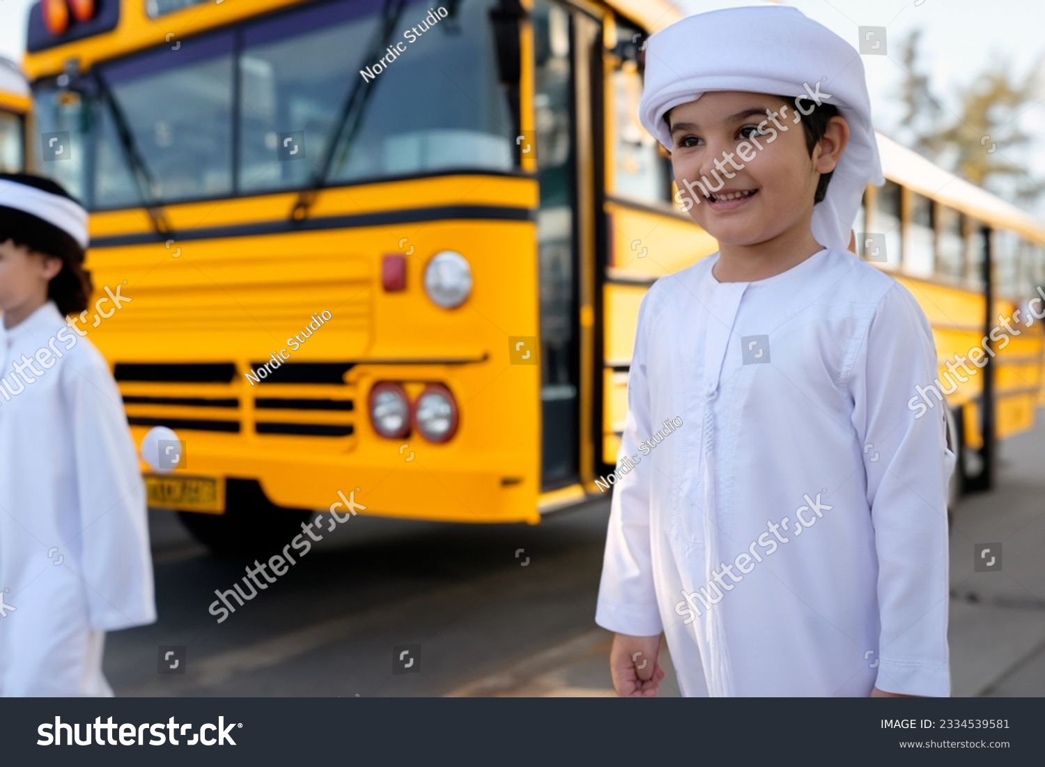 Emirati student near yellow school bus. Arabic boy in UAE kandura dishdash.  #2334539581