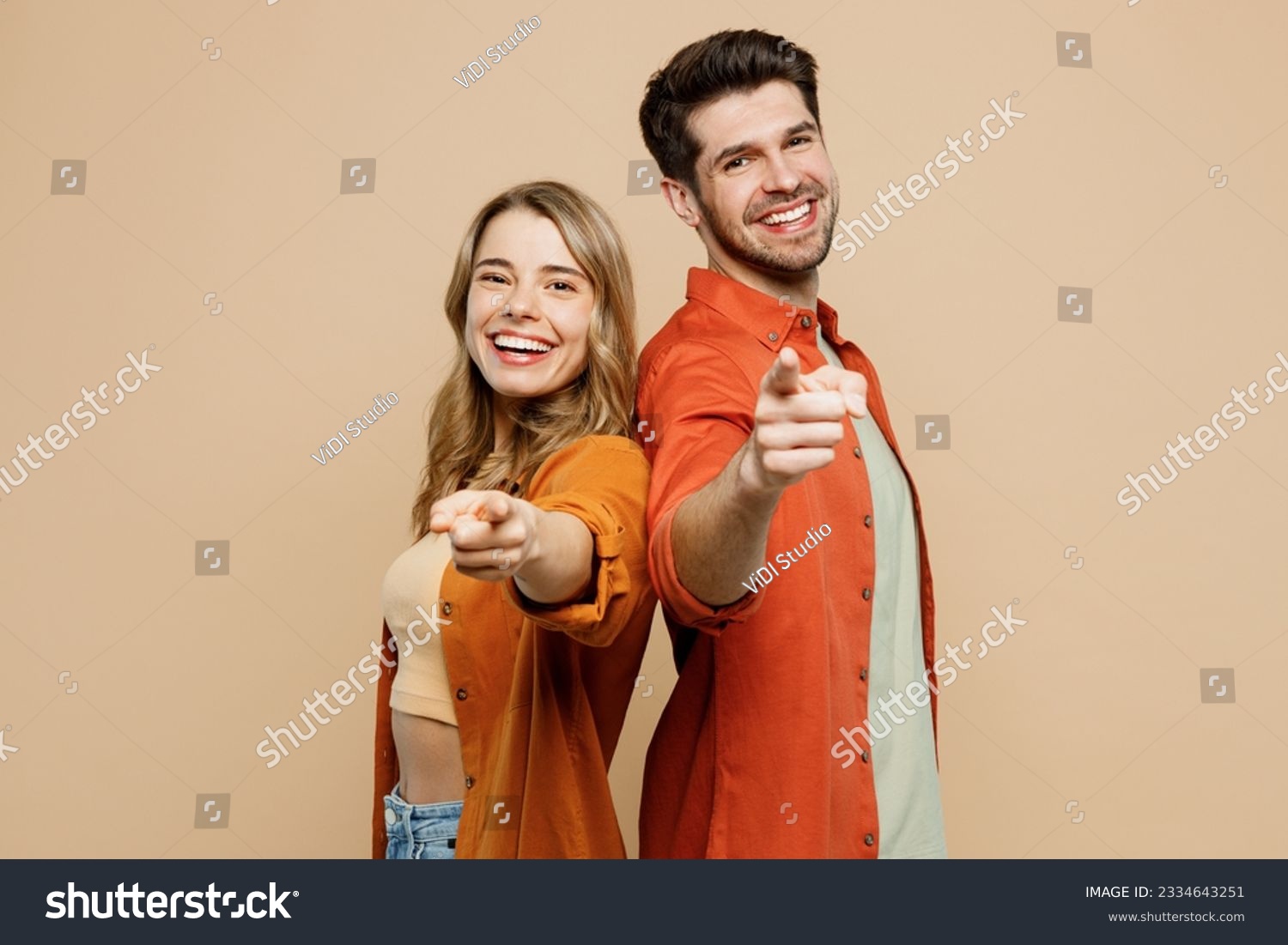 Side view young couple two friends family man woman wear casual clothes point index finger camera you stand back to back together isolated on pastel plain light beige color background studio portrait #2334643251