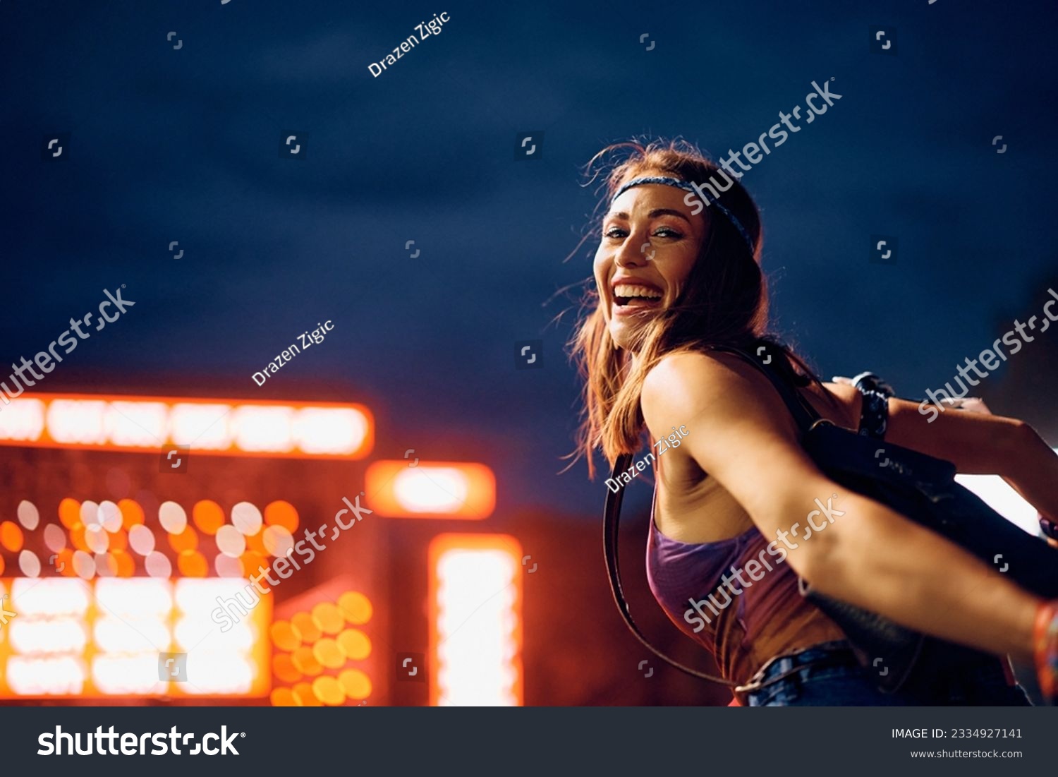 Happy woman having fun while attending open air music concert at night and looking at camera.  #2334927141