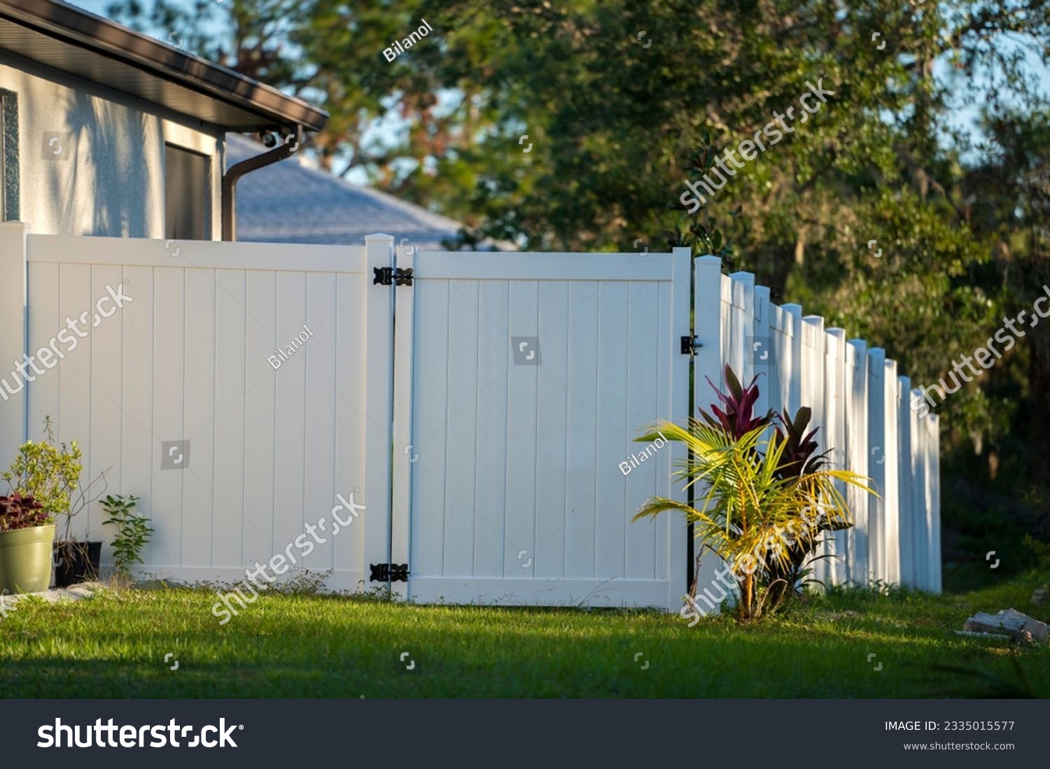 White vinyl picket fence on green lawn surrounding property grounds for backyard protection and privacy #2335015577