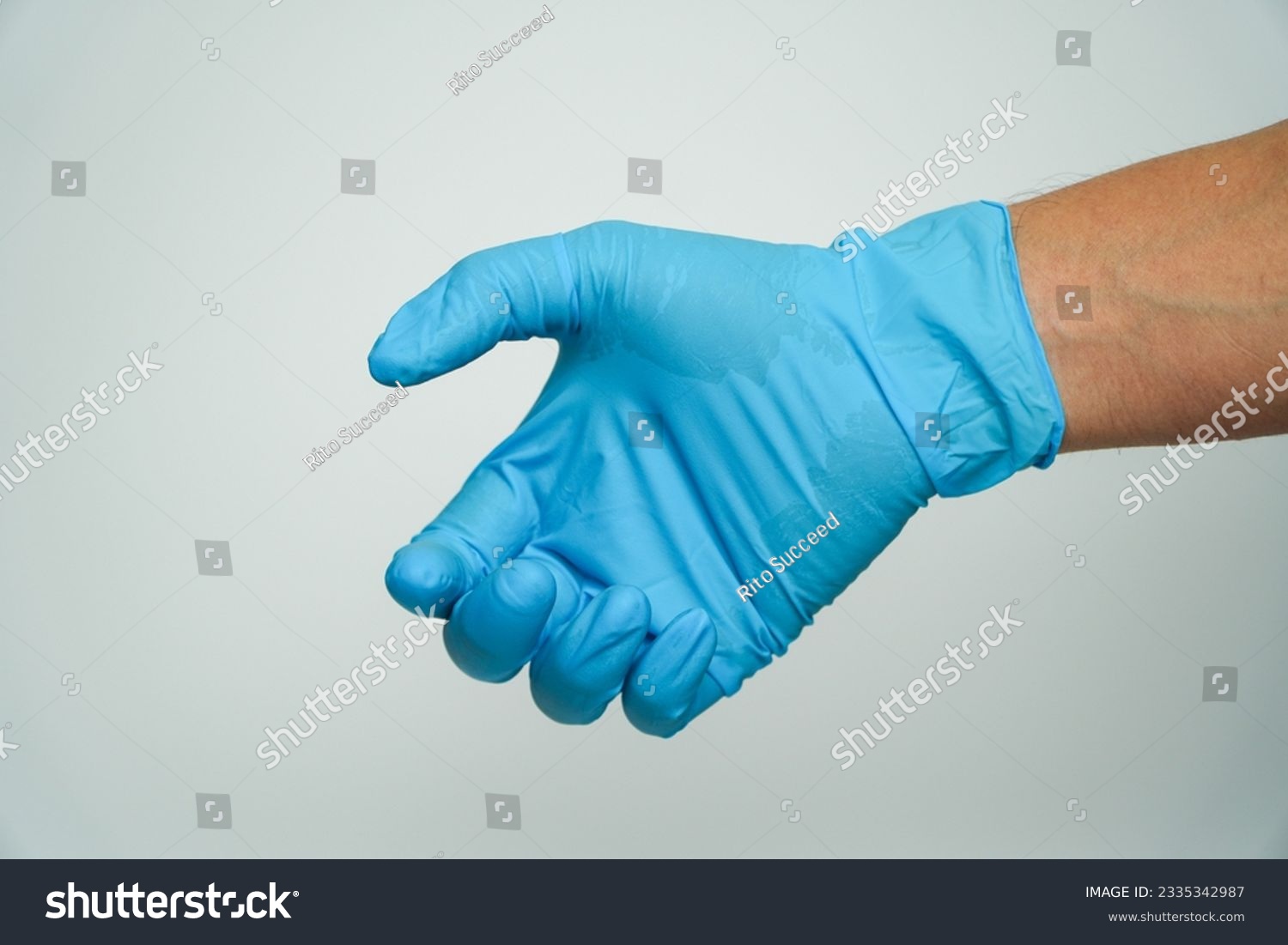 Person in blue latex gloves holding something against on a gray background,Hand in blue glove. #2335342987