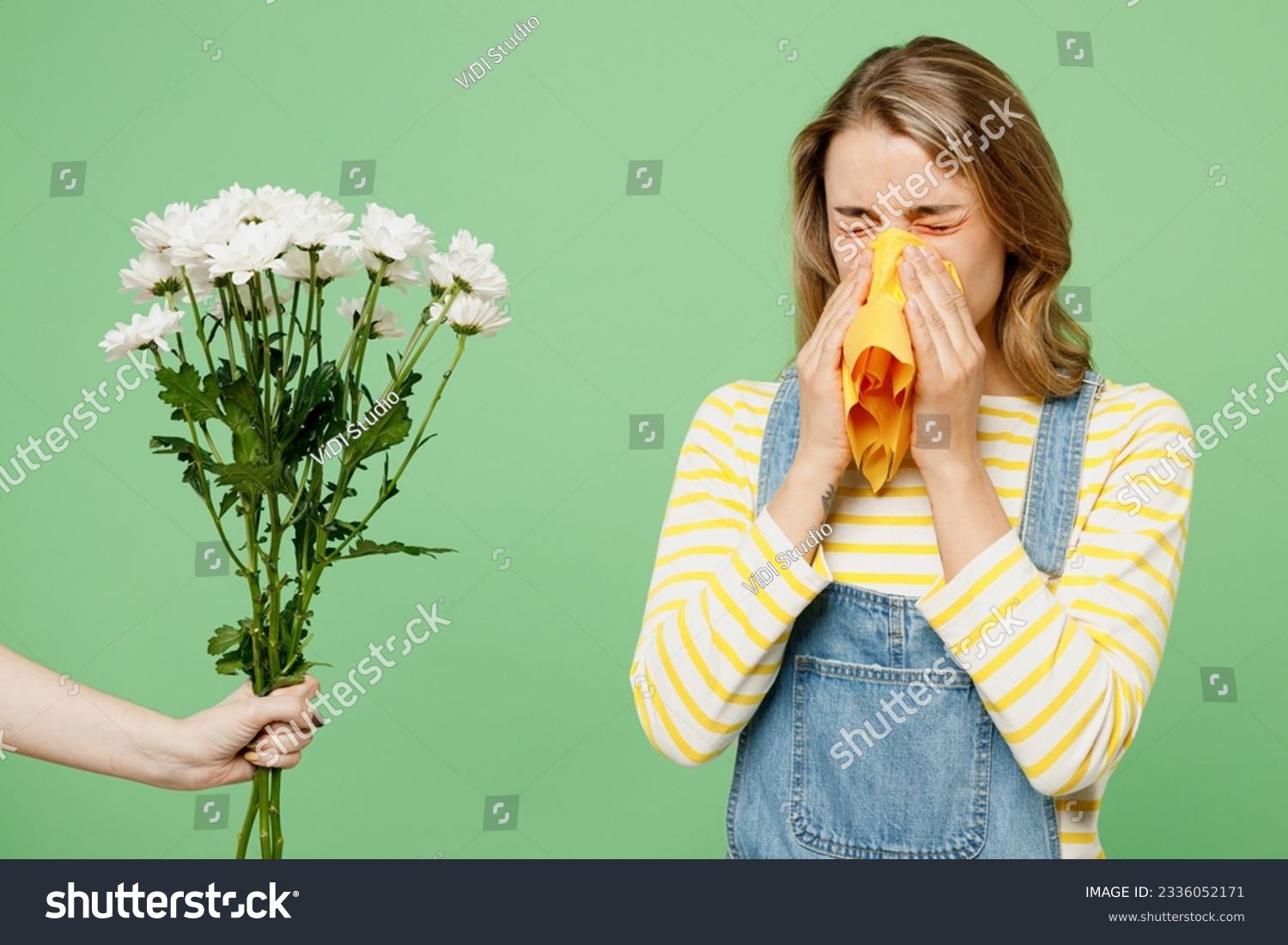 Sick unhealthy ill allergic woman has red watery eyes suffer from allergy trigger symptoms hay fever hold napkin flowers blow runny stuffy sore nose isolated on plain green background studio portrait #2336052171