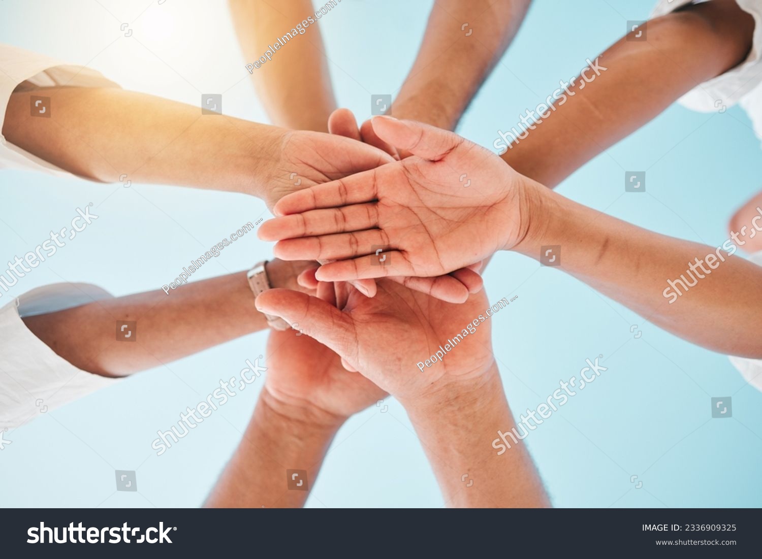 Circle, low angle and team with hands together for collaboration, unity or support by a blue sky. Teamwork, diversity and group of people in an outdoor huddle for motivation, solidarity or community. #2336909325