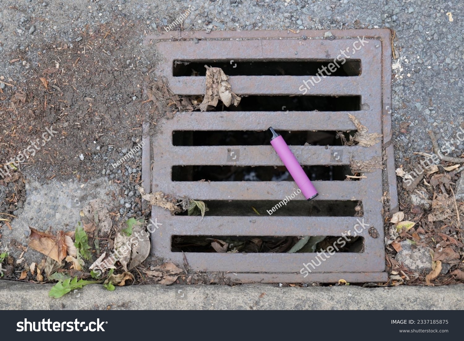 A purple e-cigarette vape has been discarded and left lying on a metal water drain cover. #2337185875