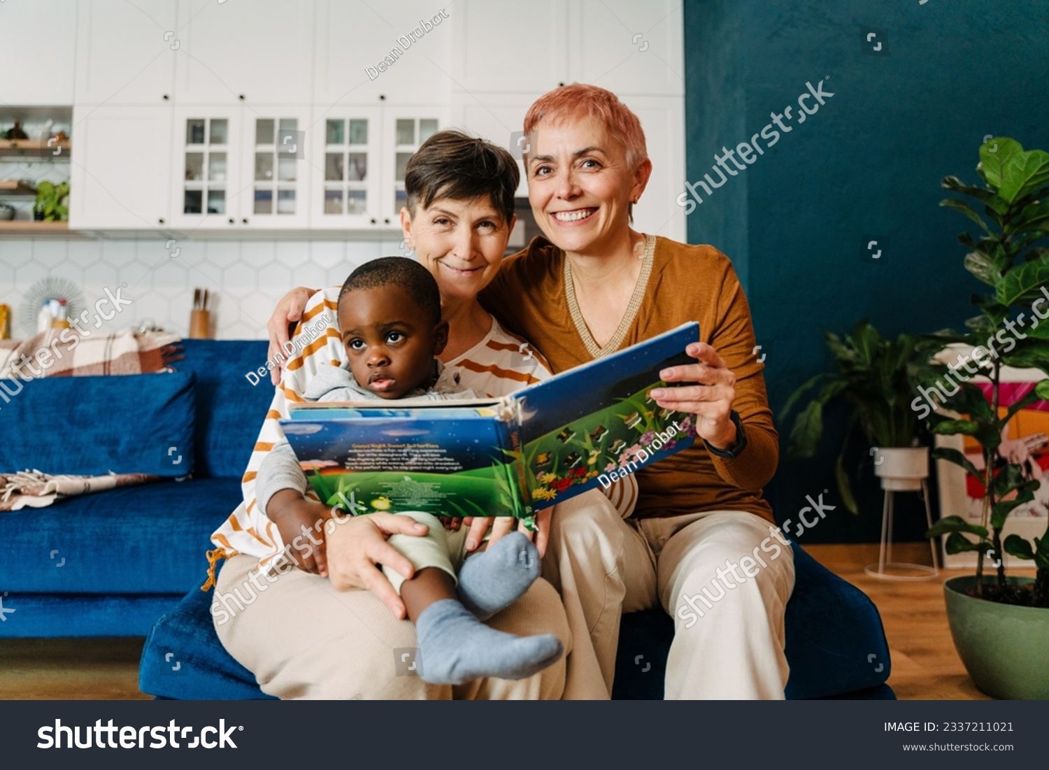 Mature lesbian couple reading book with their adopted child at home #2337211021