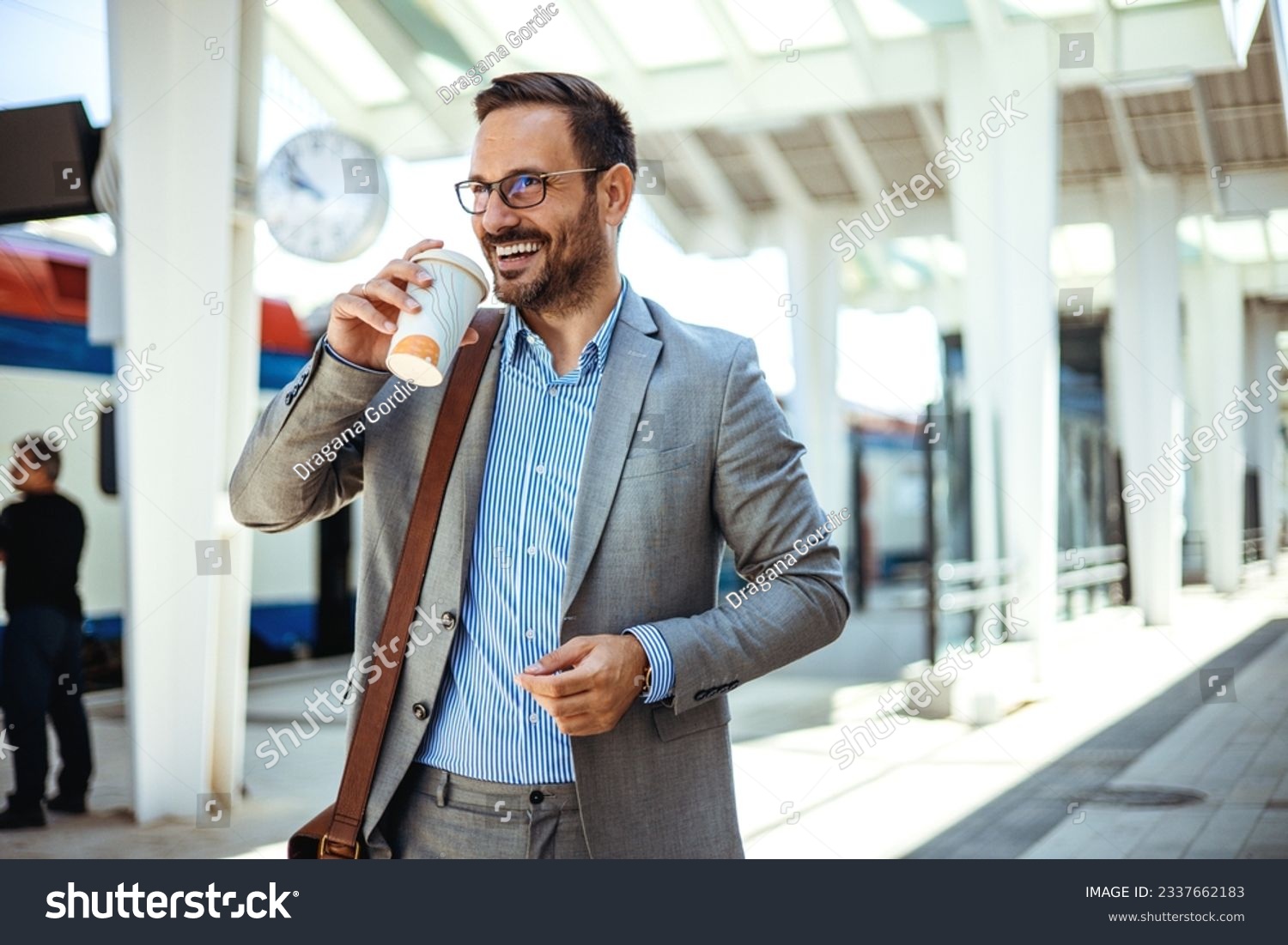 Businessman holding a disposable coffee cup at the train station platform. A man in a train station commuting to work. Businessman with coffee cup. Business person is waiting for train  #2337662183