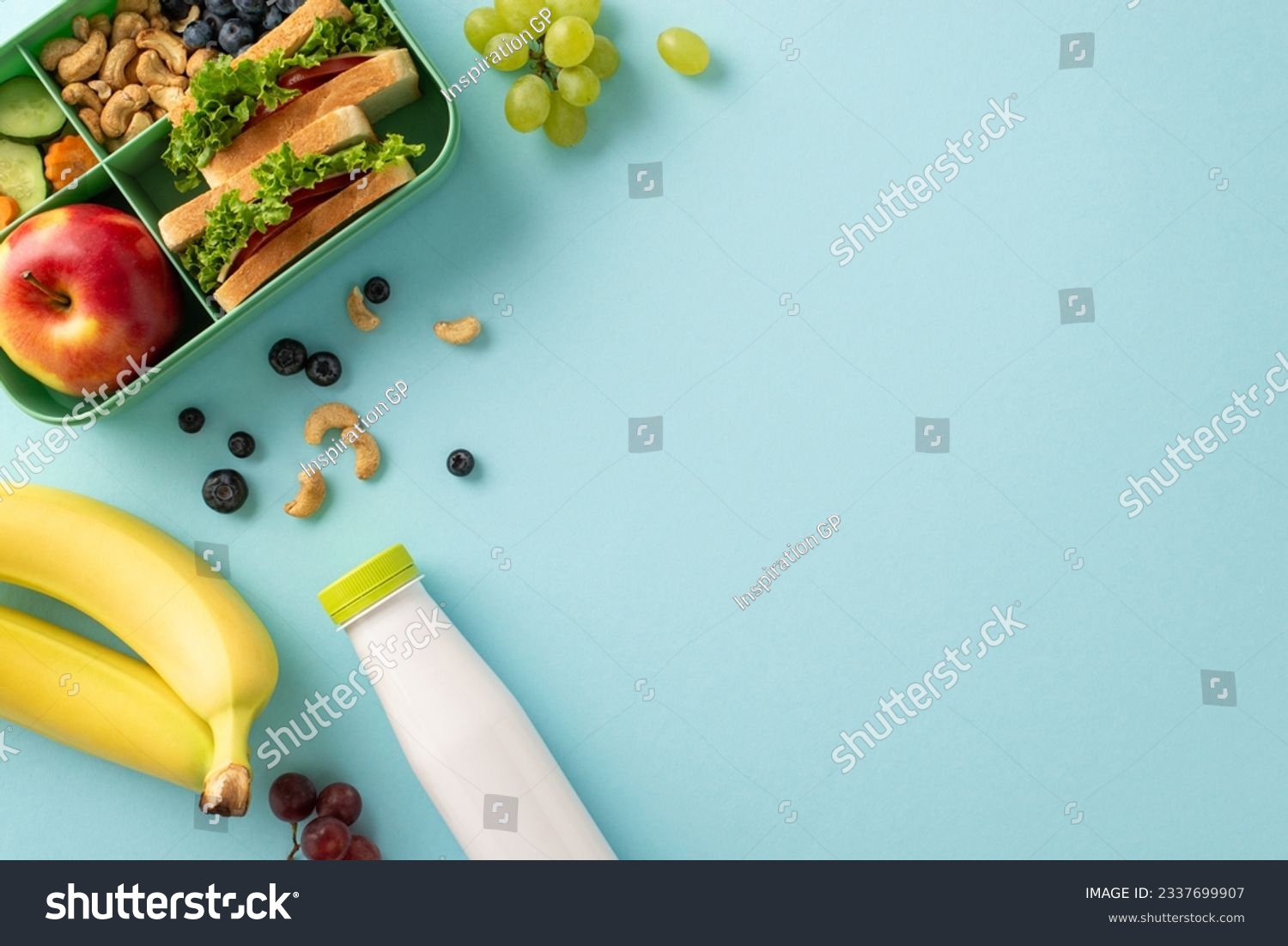 Wholesome lunchtime concept portrayed from a top-down view. The lunchbox holds nutritious sandwiches, fruits, buts and berries on blue isolated background, offering copyspace for text or promotions #2337699907