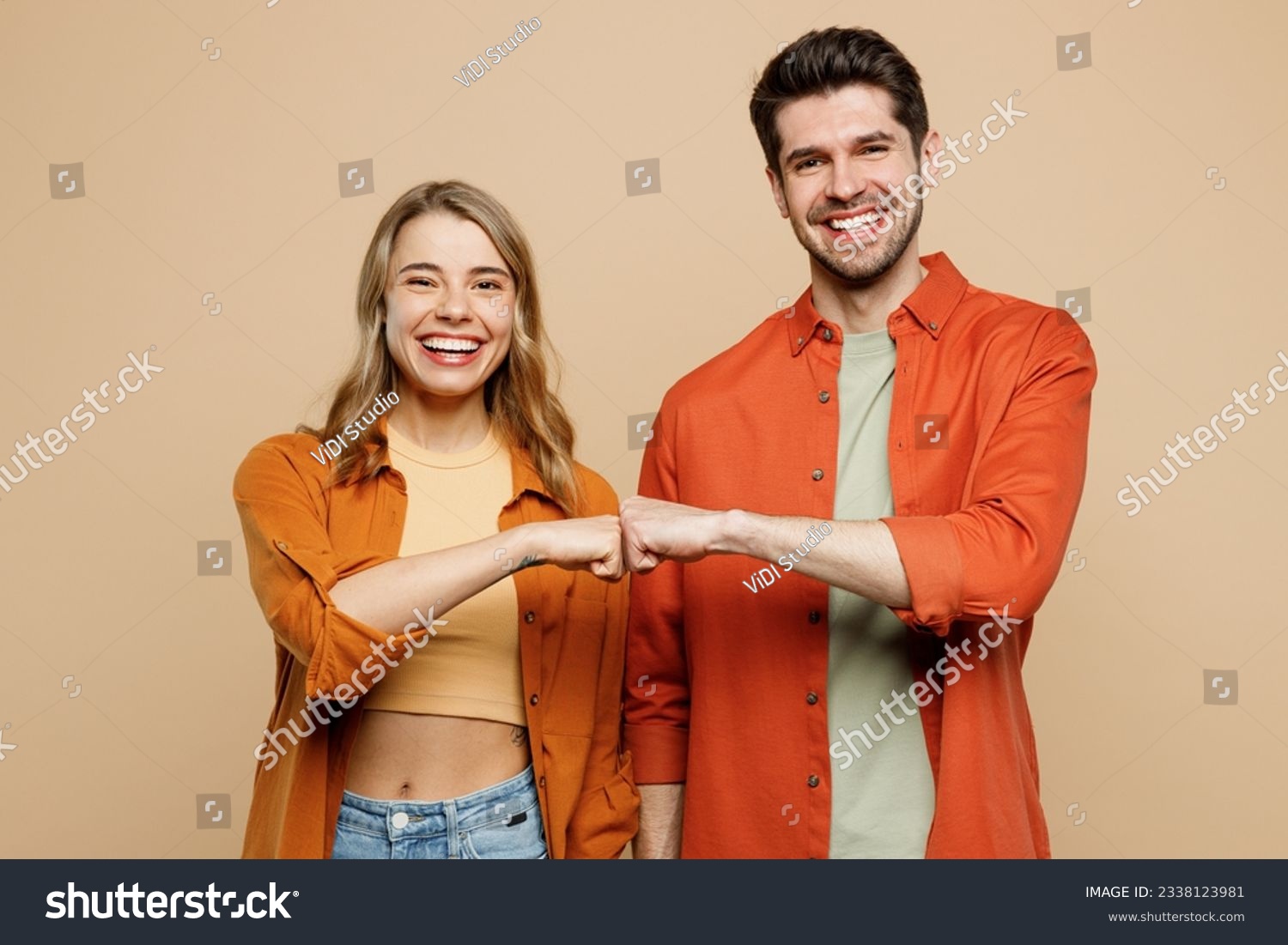 Young smiling happy buddies fun couple two friends family man woman wear casual clothes looking camera giving fist bumo together isolated on pastel plain light beige color background studio portrait #2338123981
