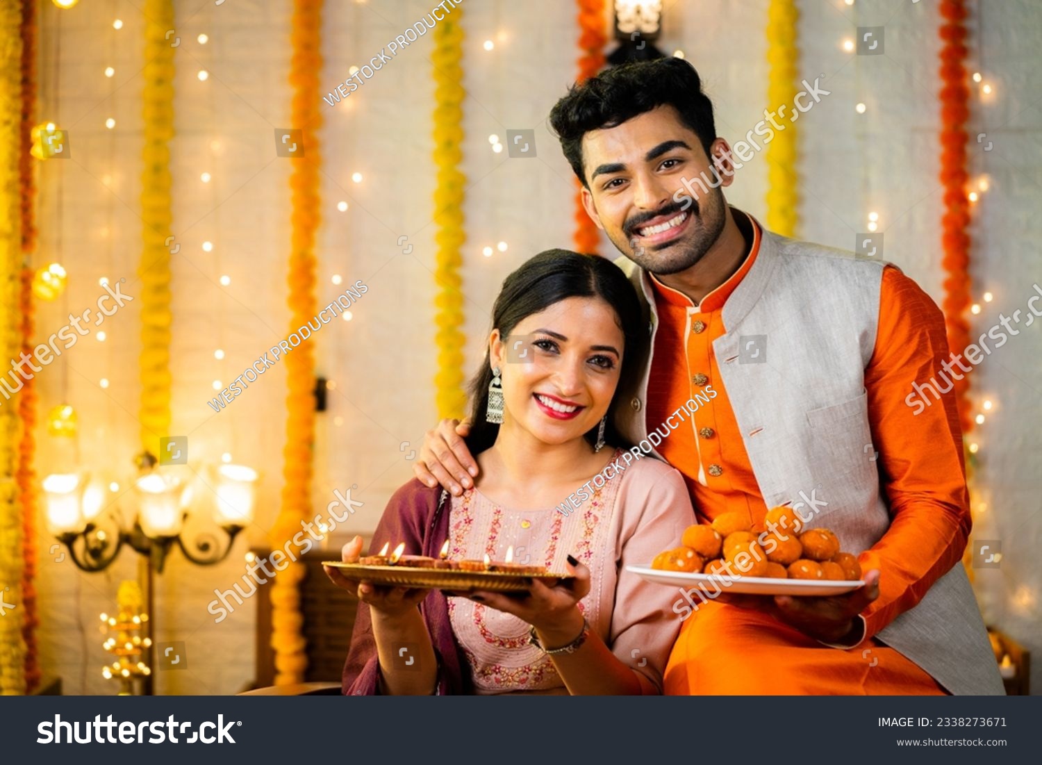 Happy smiling indian couple in traditional ethnic wear by holding sweets at home - concept of diwali festive celebration, greeting and family relationship #2338273671
