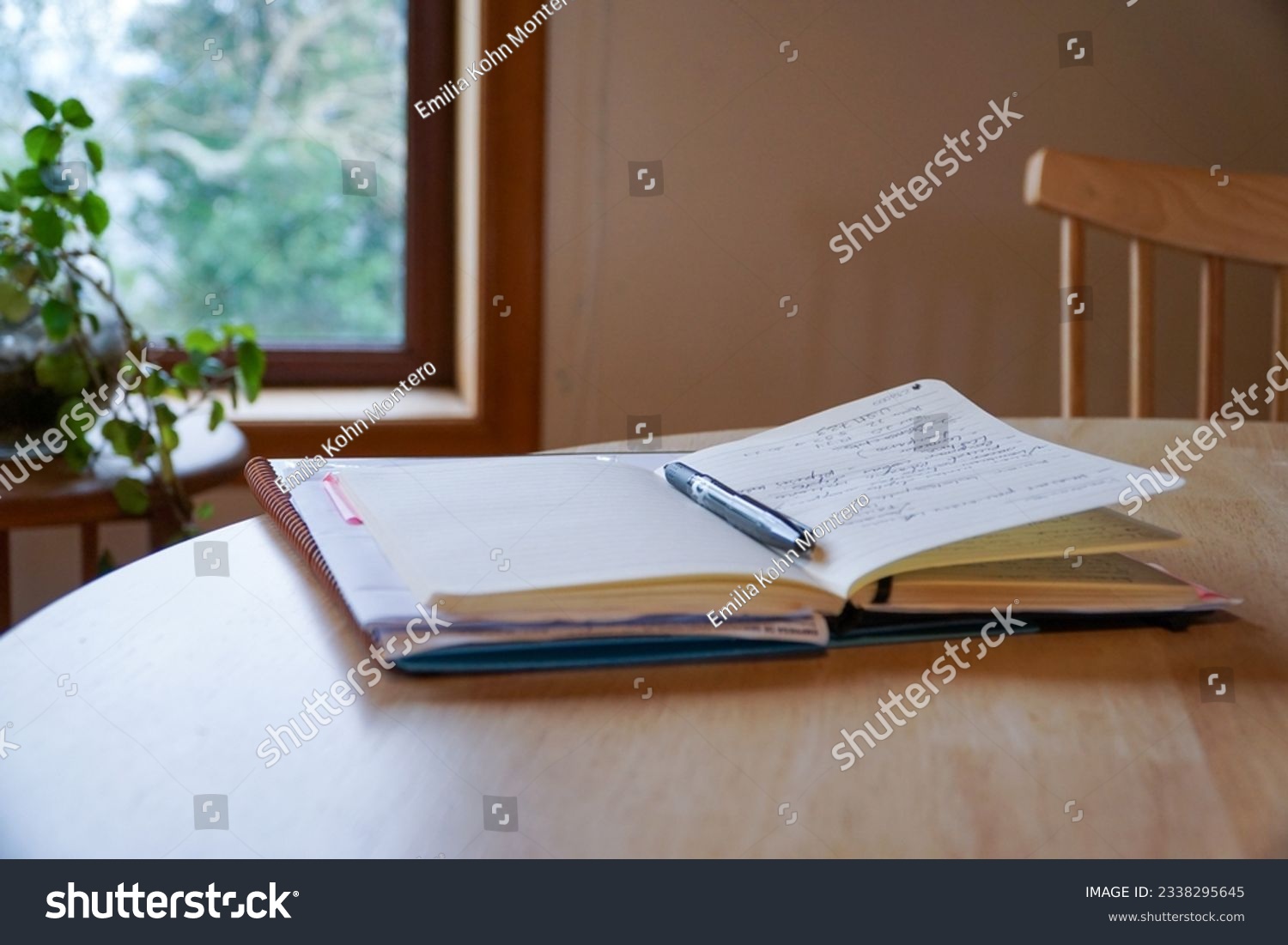 An open notebook with a pencil placed on top, resting on a wooden table inside the house, symbolizing creativity and ideas in a cozy home setting. #2338295645