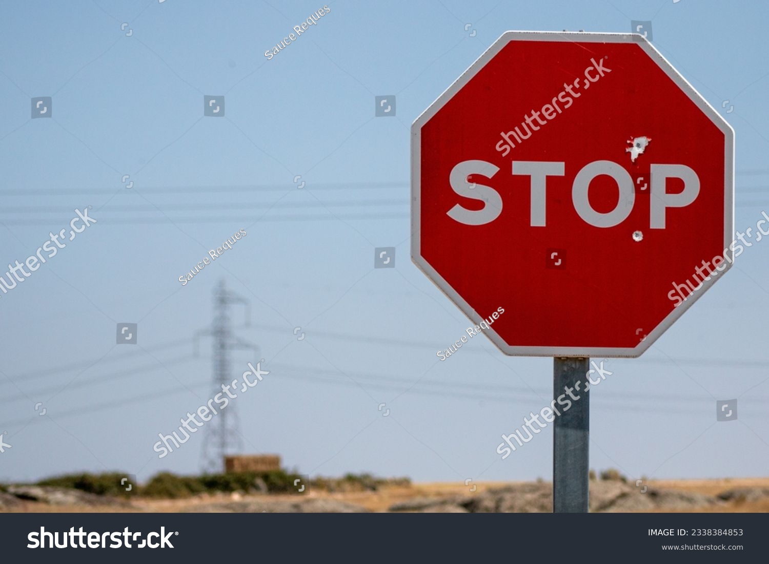 Stop sign, which has been shot with a firearm, in the background you can see cables and an electric tower. Concept: prohibited, demand power station #2338384853