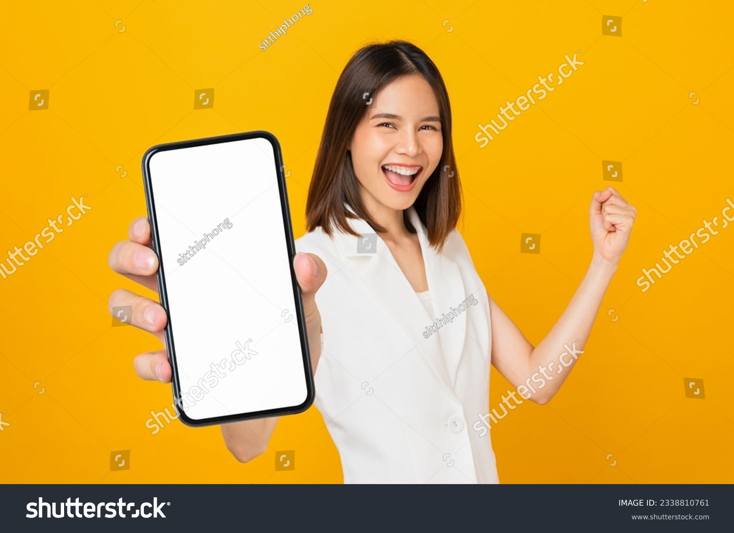 Beautiful Asian woman holding smartphone mockup of blank screen and smiling on yellow background. #2338810761