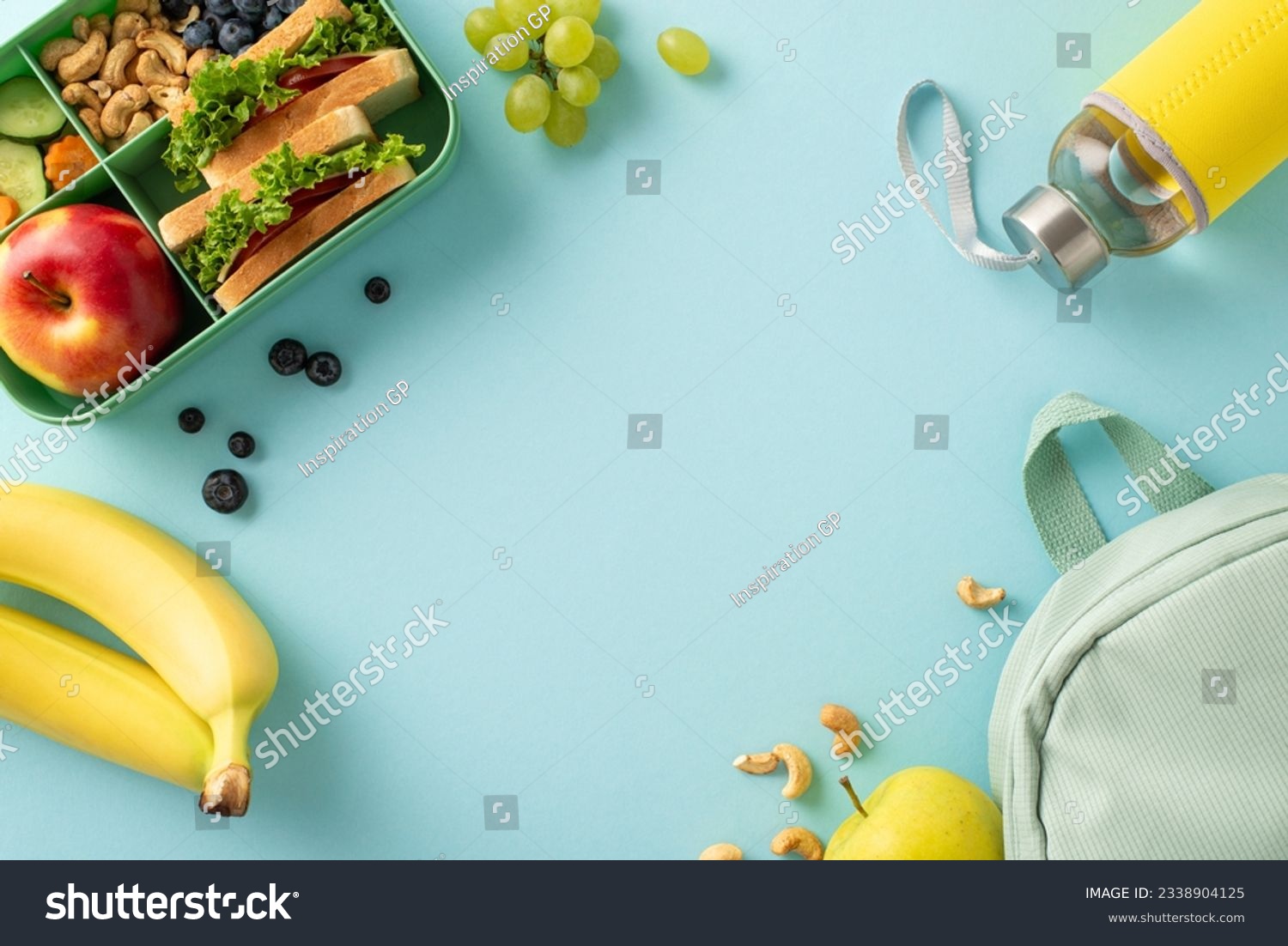 A nourishing school break scene from above, displaying a lunchbox with sandwiches accompanied by fruits, berries, water bottle and rucksack on blue isolated backdrop, perfect for text or advertising #2338904125