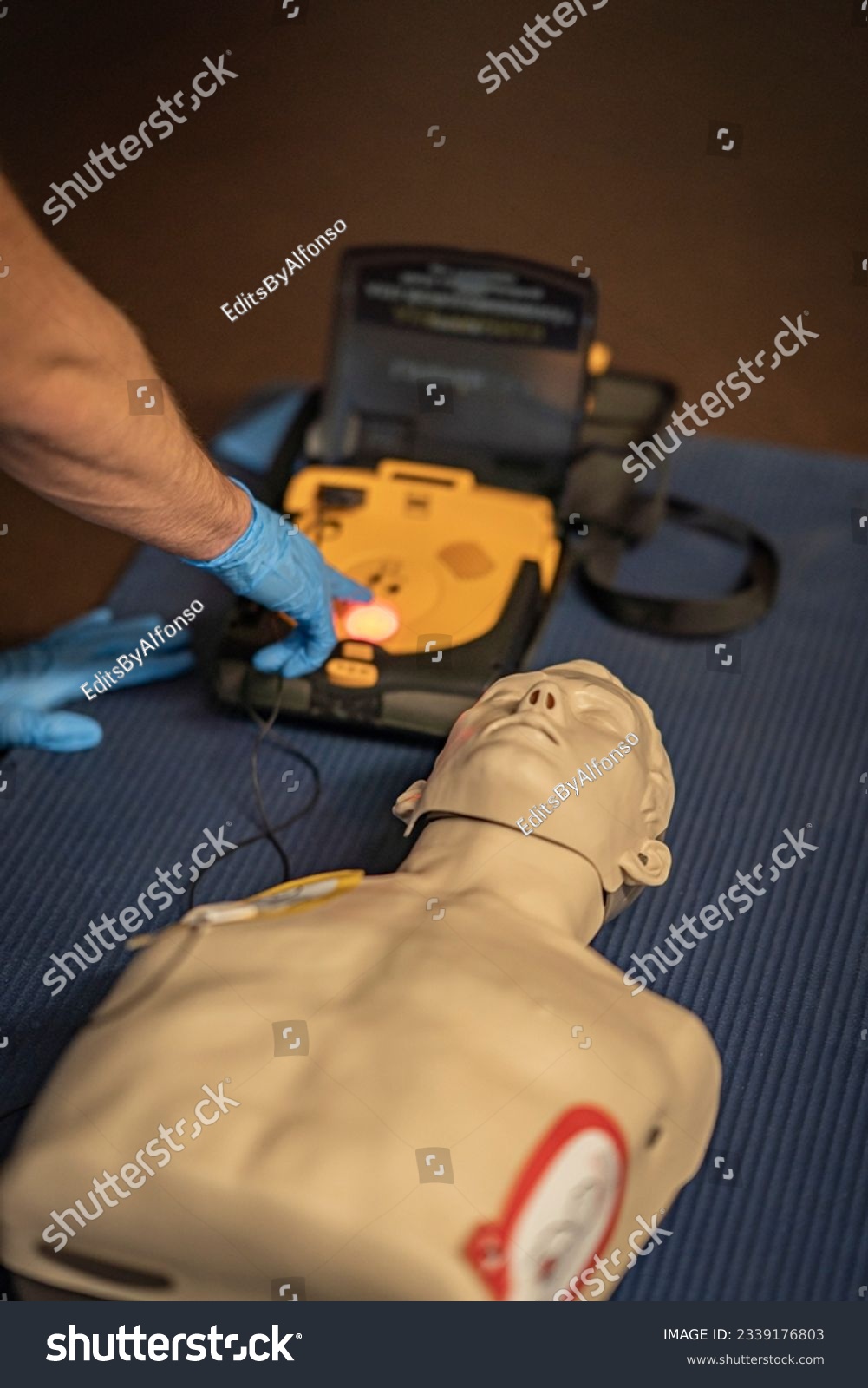 First aid training – The resusitation has started. The instructor ist going to activate the shock. The shock discharge button flashes red. The AED is loaded and the patient is now being shocked. #2339176803