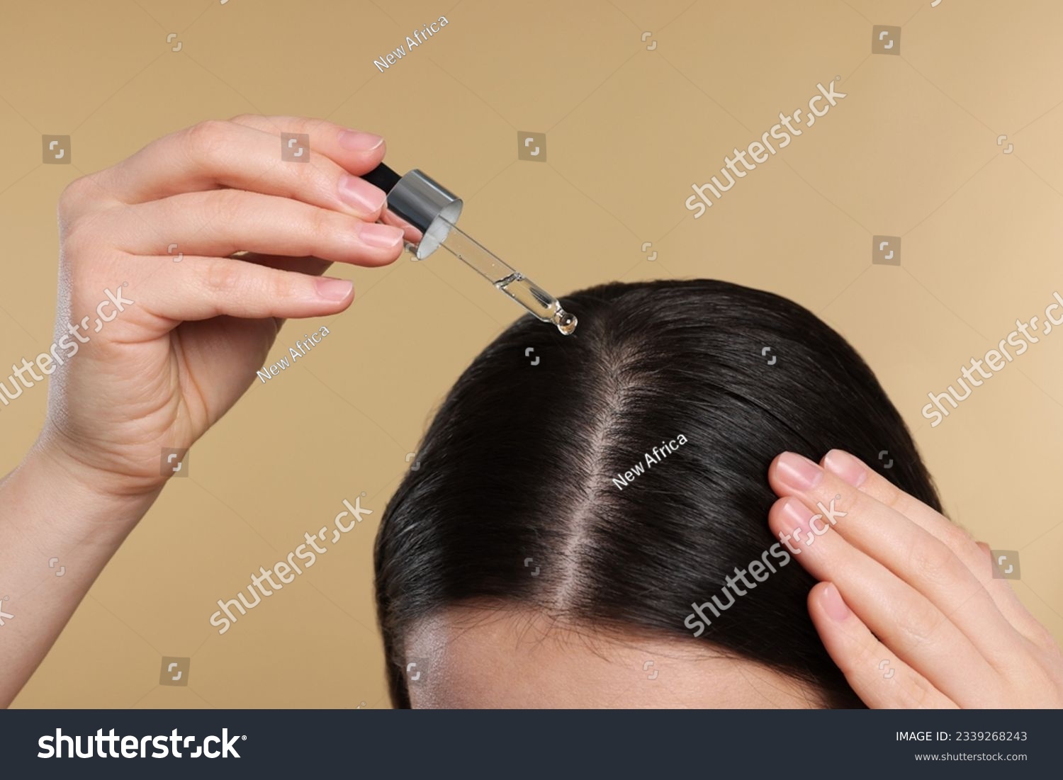 Woman applying essential oil onto hair roots on beige background, closeup #2339268243