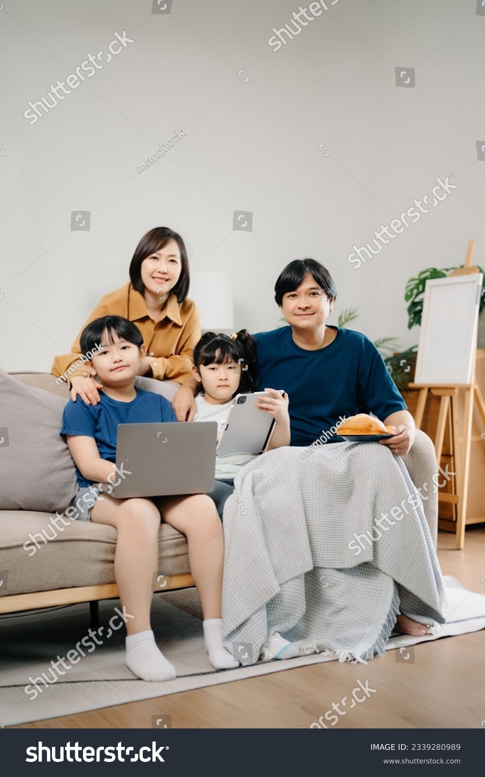 Asian Overjoyed kids sitting on sofa with cheerful parents, watching funny video on computer. Happy married couple enjoying spending weekend time with children, looking at laptop and tablet  #2339280989