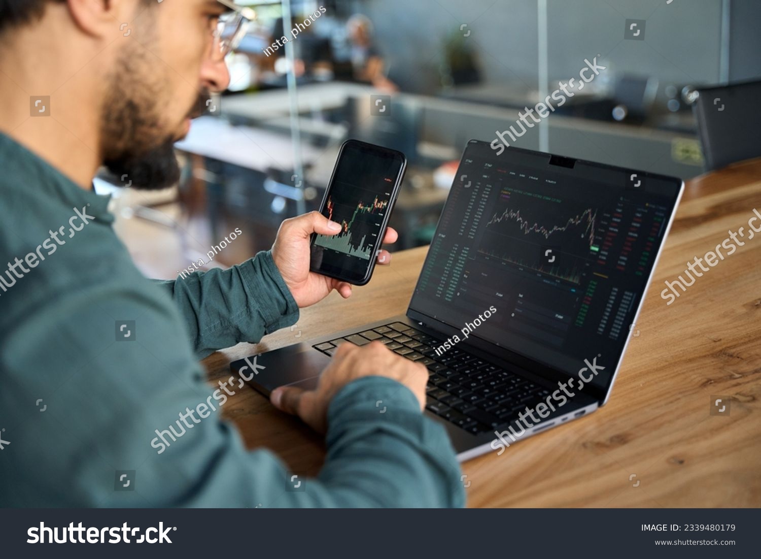 Investor using mobile phone and laptop checking trade market data. Stock trader broker looking at computer analyzing trading cryptocurrency finance market crypto stockmarket data, over shoulder view. #2339480179