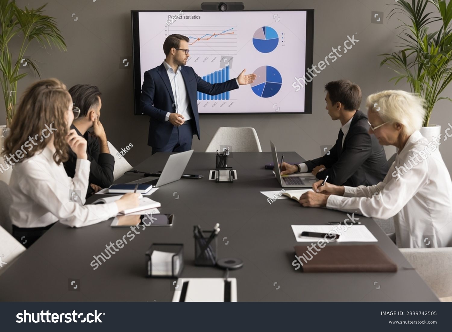 Confident young business leader man presenting marketing statistic report to partners, investors, selling startup project on meeting, negotiations, showing graphs on electronic display #2339742505