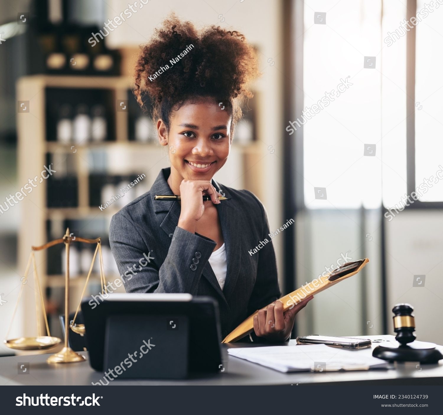 African american lawyer woman in suit holding envelope of business contract and reading information on tablet while sitting to working about legal and justice with judge hammer on desk in courtroom. #2340124739