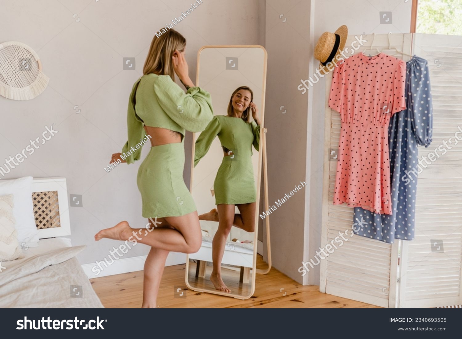 young pretty woman in green dress trying on fashion style trend dress looking in mirror at home or showroom #2340693505